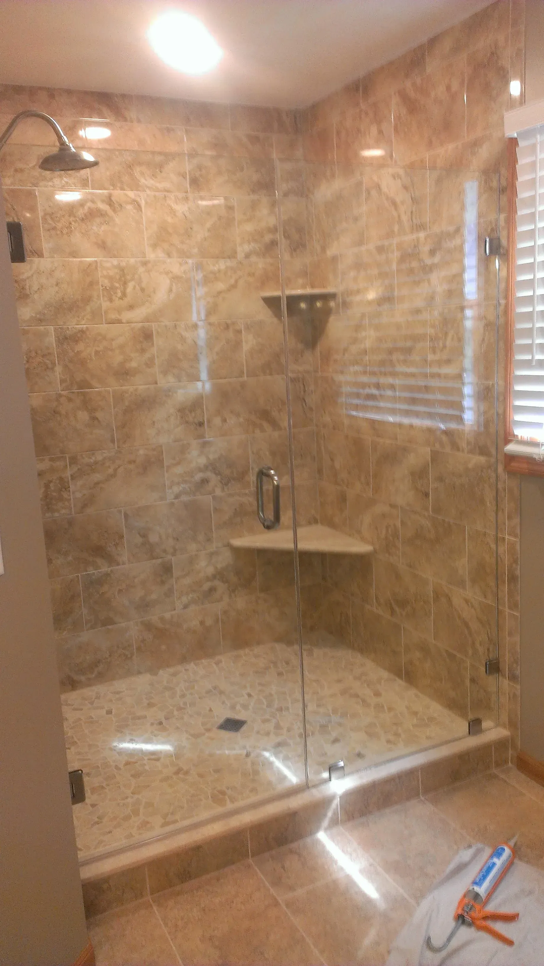 A tiled shower with glass doors, shelves, and a stone floor; bathroom interior.