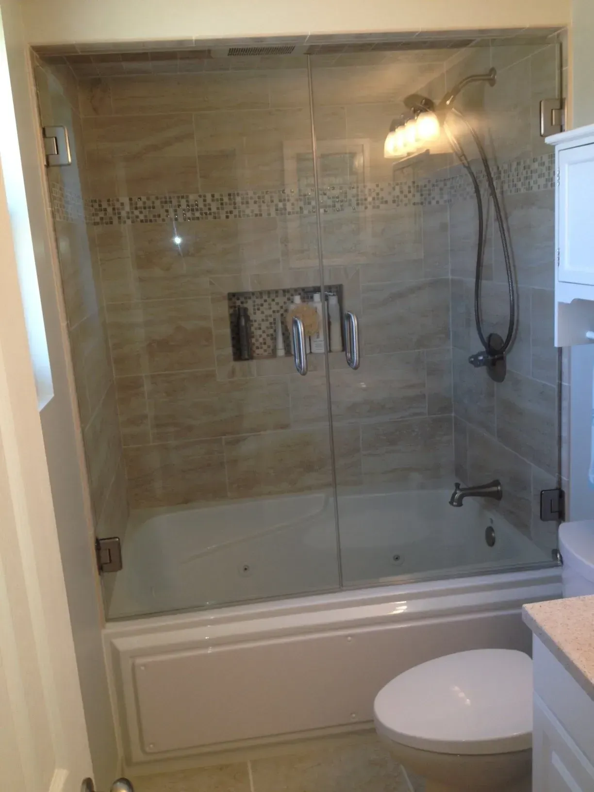 Bathroom with glass shower doors, white tub, beige tile, and a toilet.