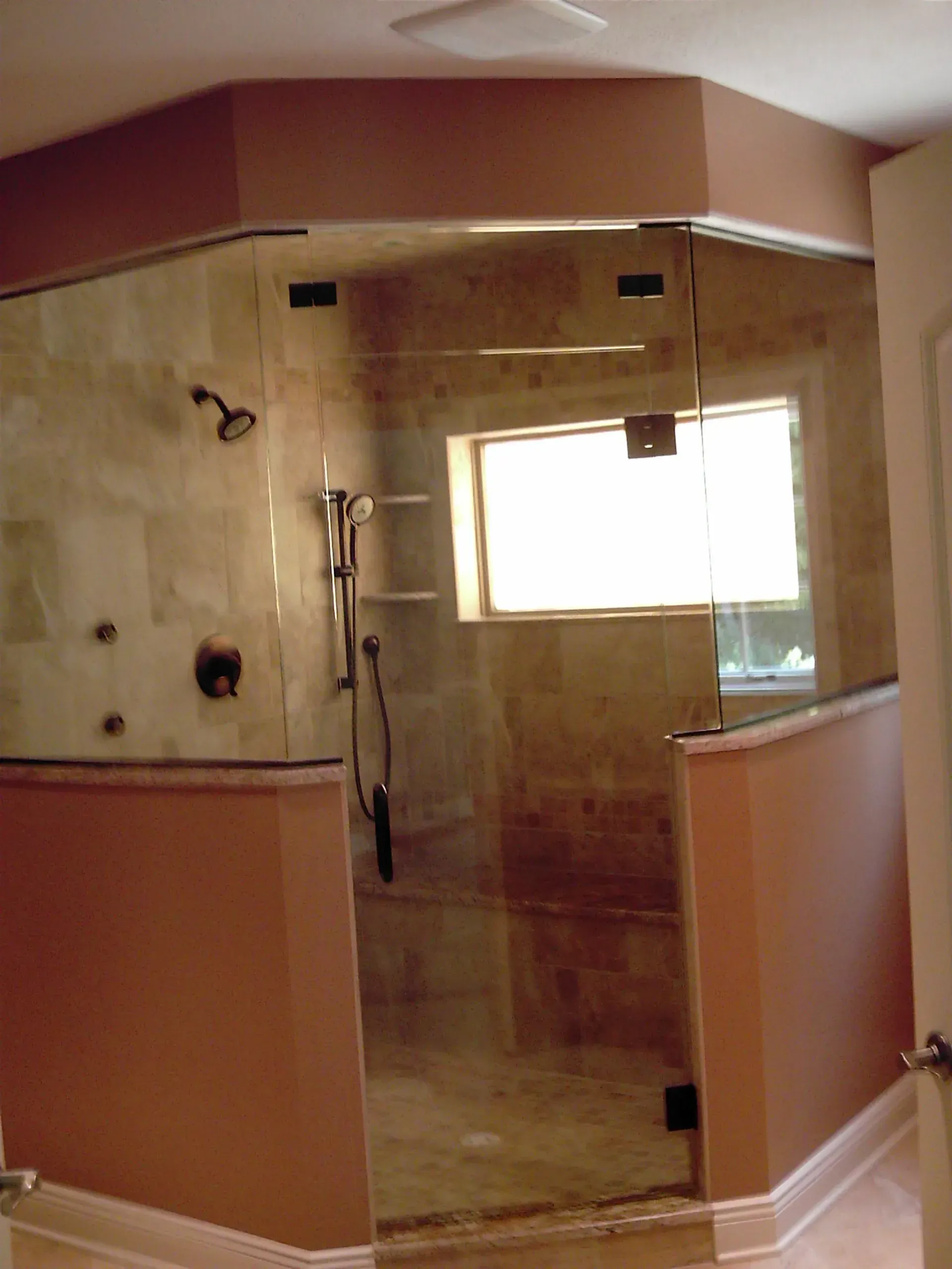 A luxurious bathroom with a glass shower enclosure, tan tile, and peach-colored walls.