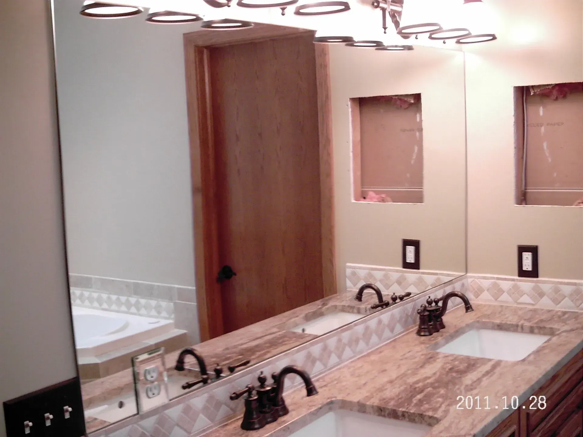 Bathroom with double sinks, mirror, beige walls, granite countertop, wooden door.