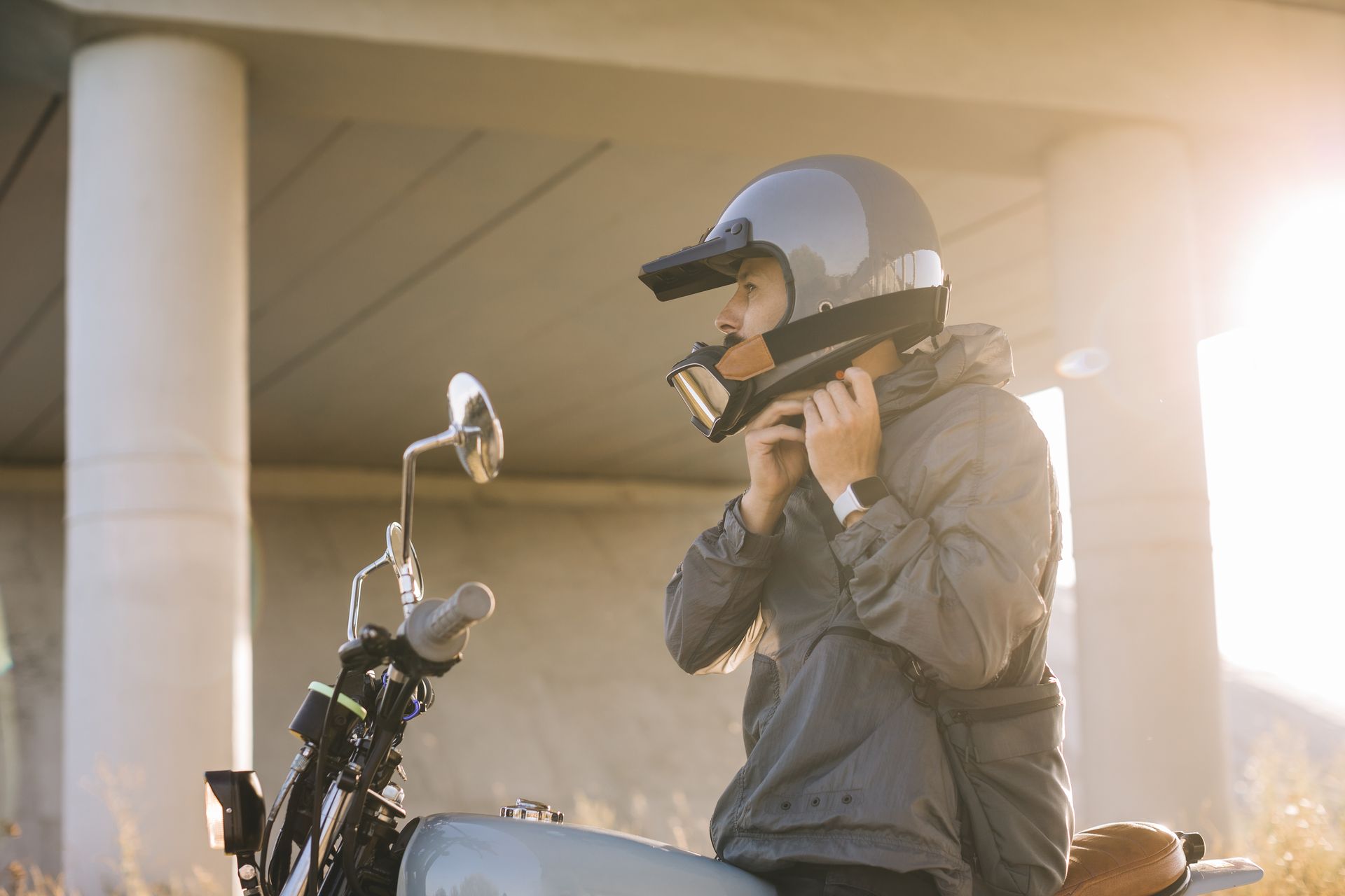 Person putting on a motorcycle helmet, sitting on a scooter outdoors.