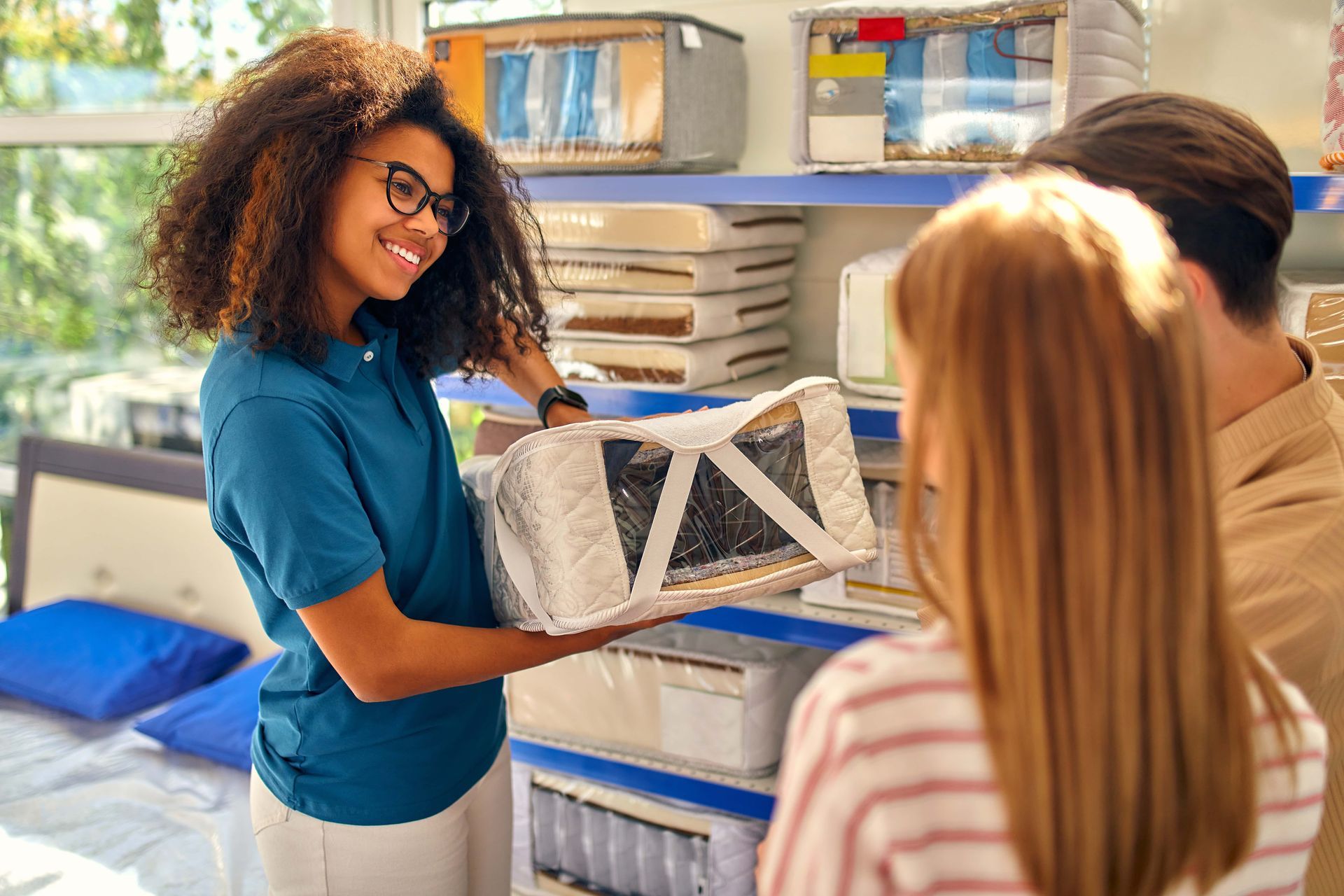 Sales associate shows a mattress to a couple in a mattress store, smiling.