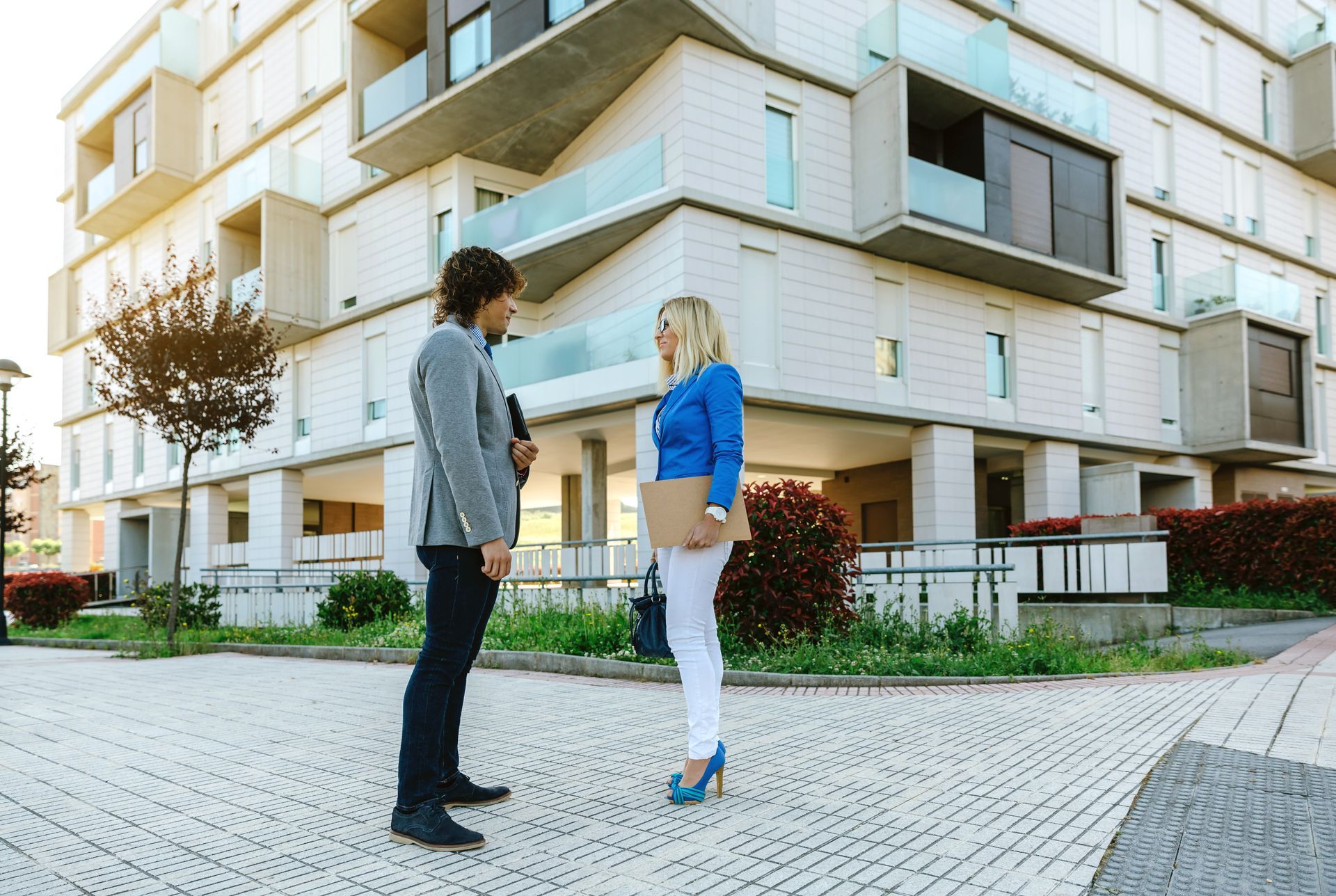 Man and woman in front of an apartment building, talking. The woman is holding a clipboard.