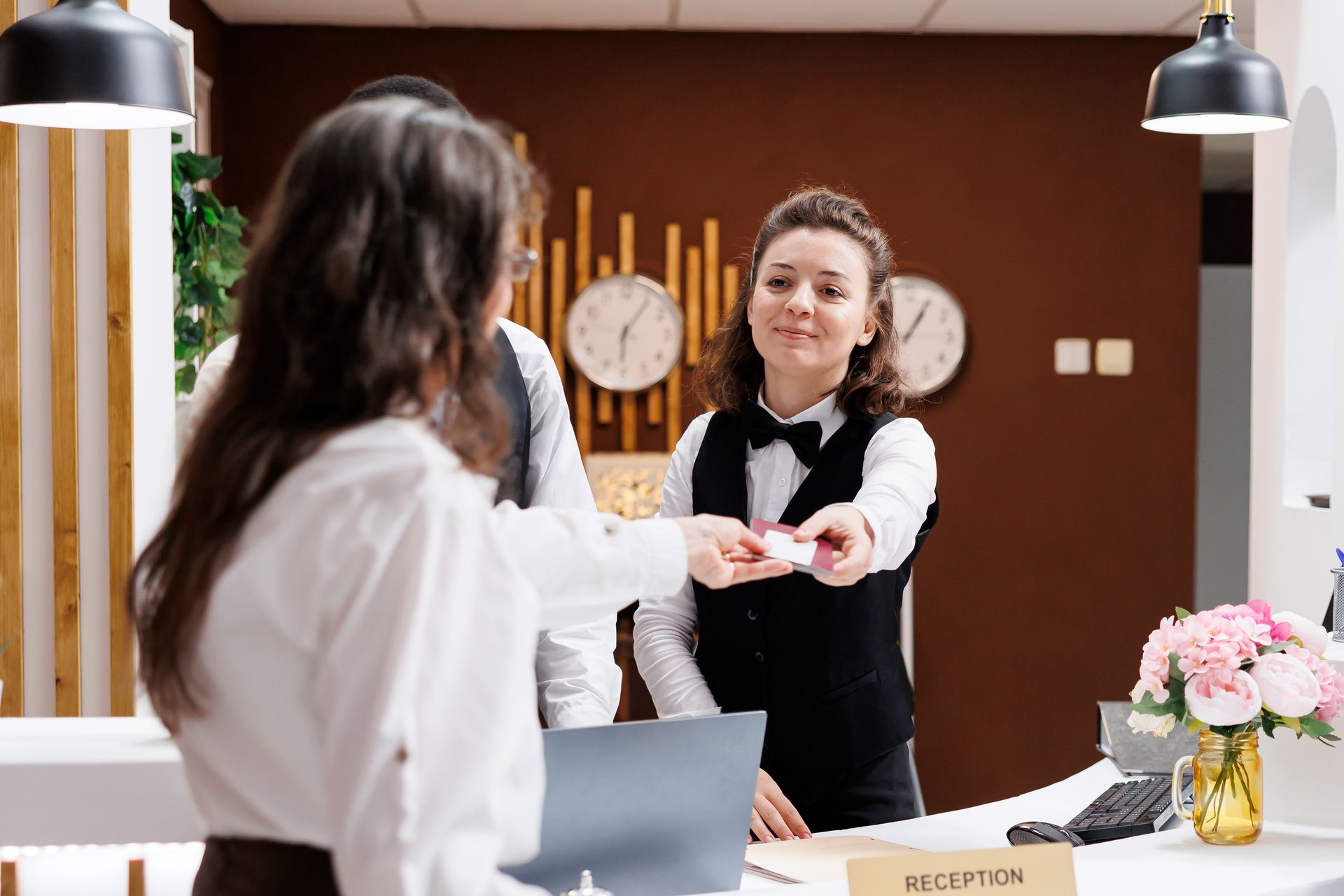 Hotel receptionist handing a key card to a guest at the front desk.