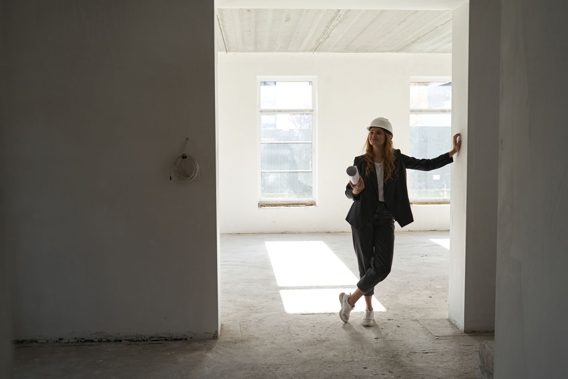 Woman in hard hat and suit leans in doorway of unfinished building.