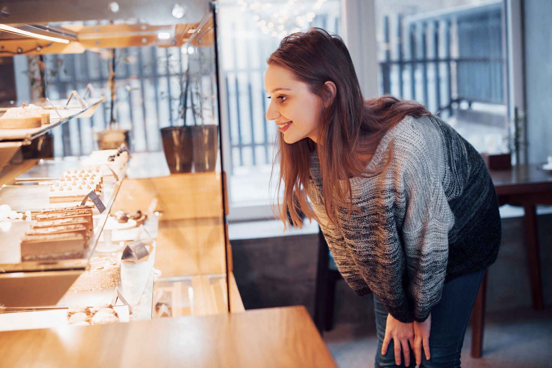 Woman smiling, looking at pastries in a glass display case at a cafe.