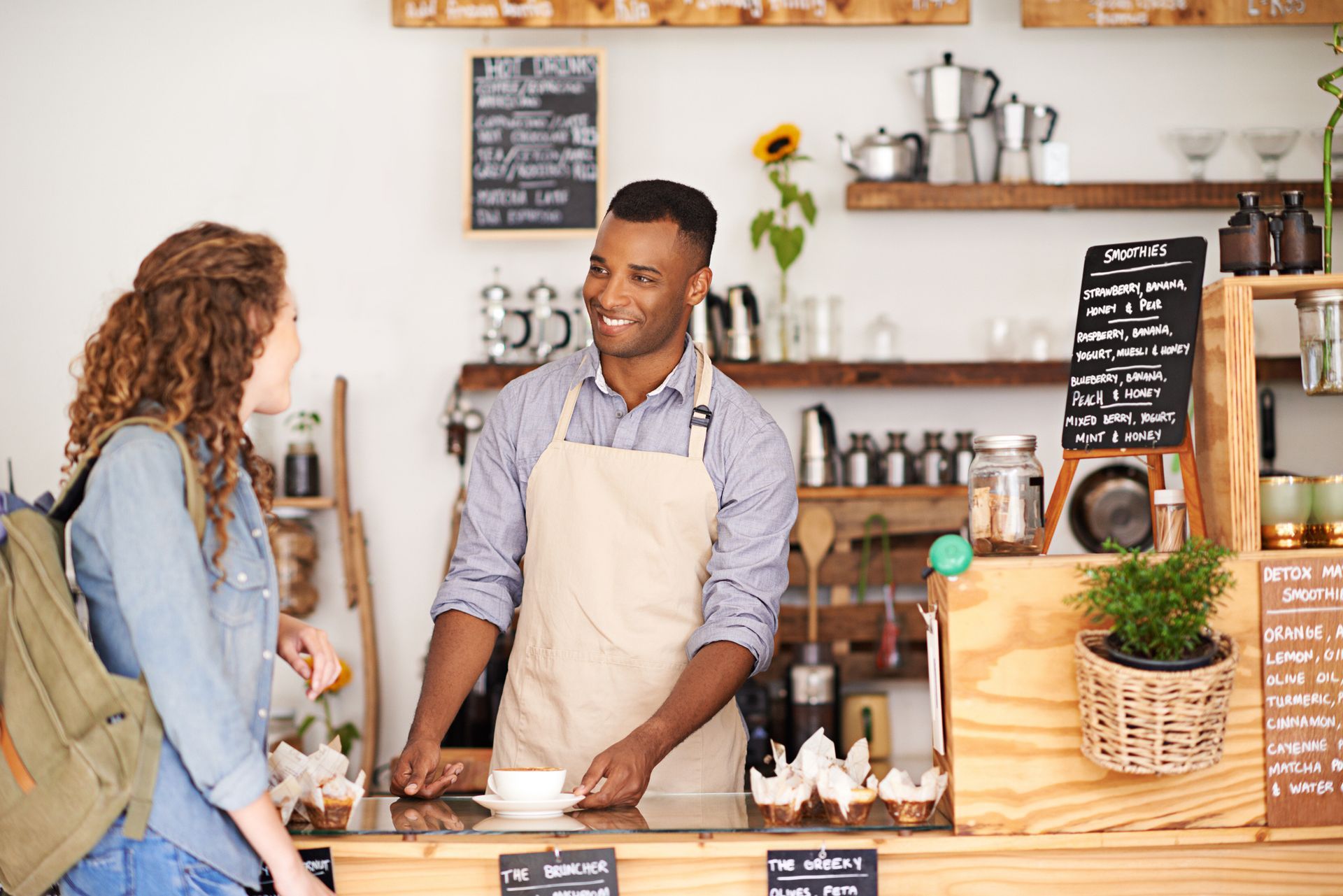 Man in apron serves a smiling woman coffee in a cafe.