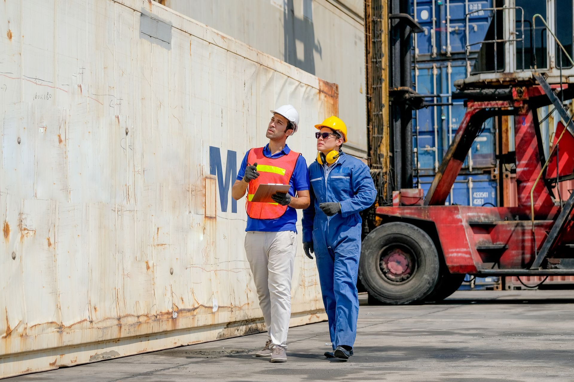 Two workers in safety gear inspect a shipping container at a port.