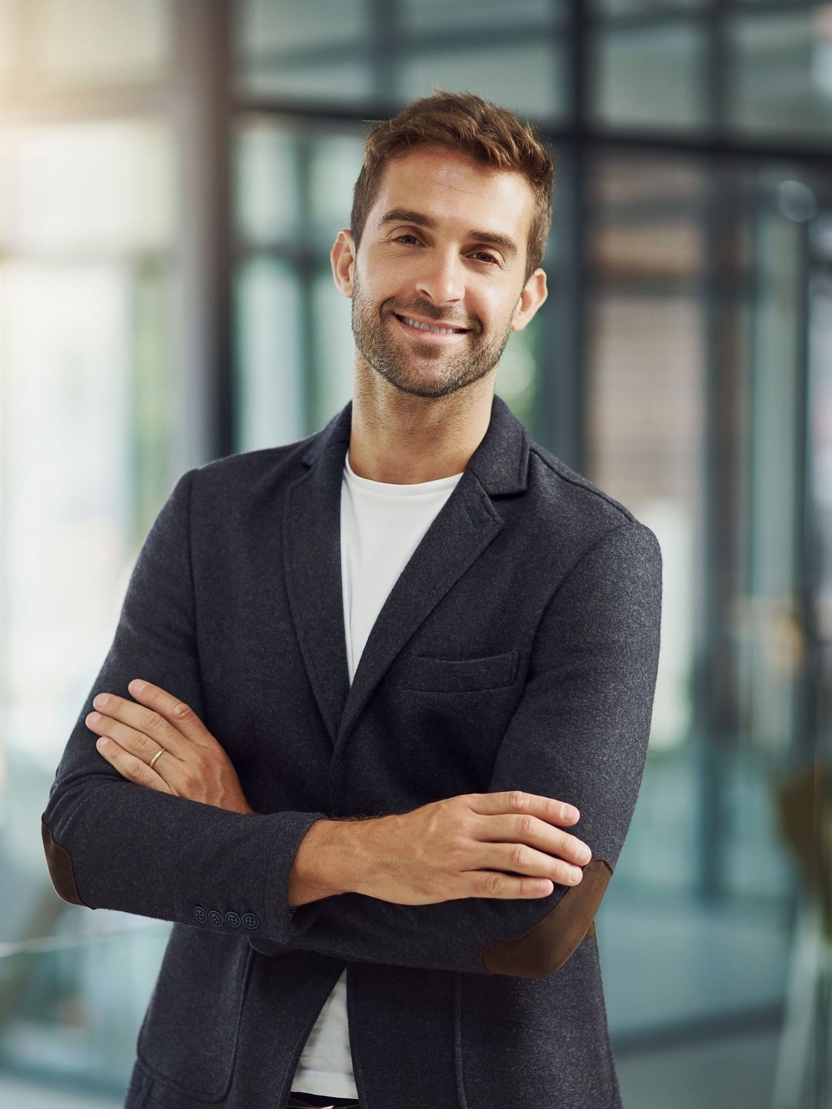 Man in blazer with arms crossed, smiling in an office setting.