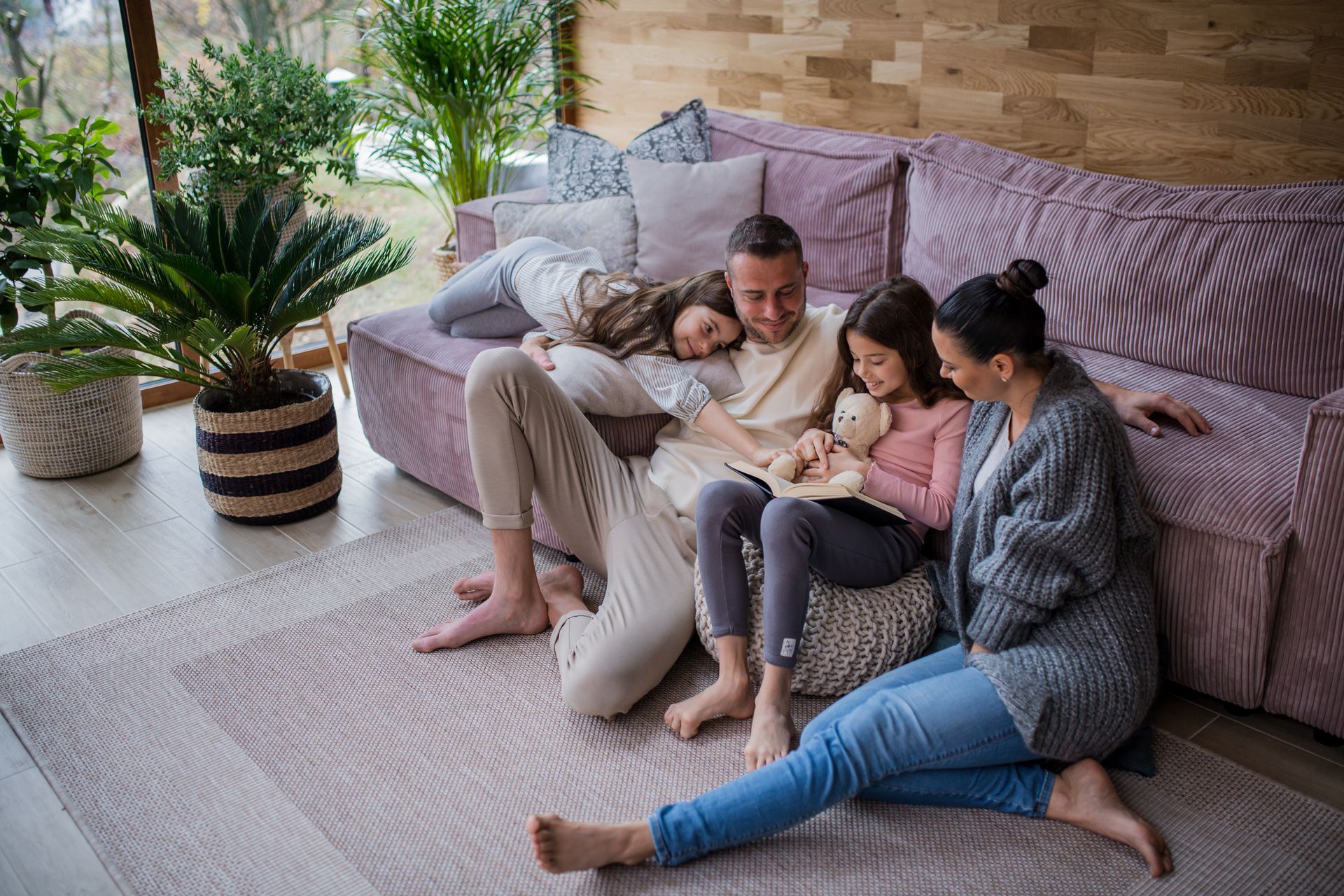 Family of five cuddling on a couch and rug in a bright living room.