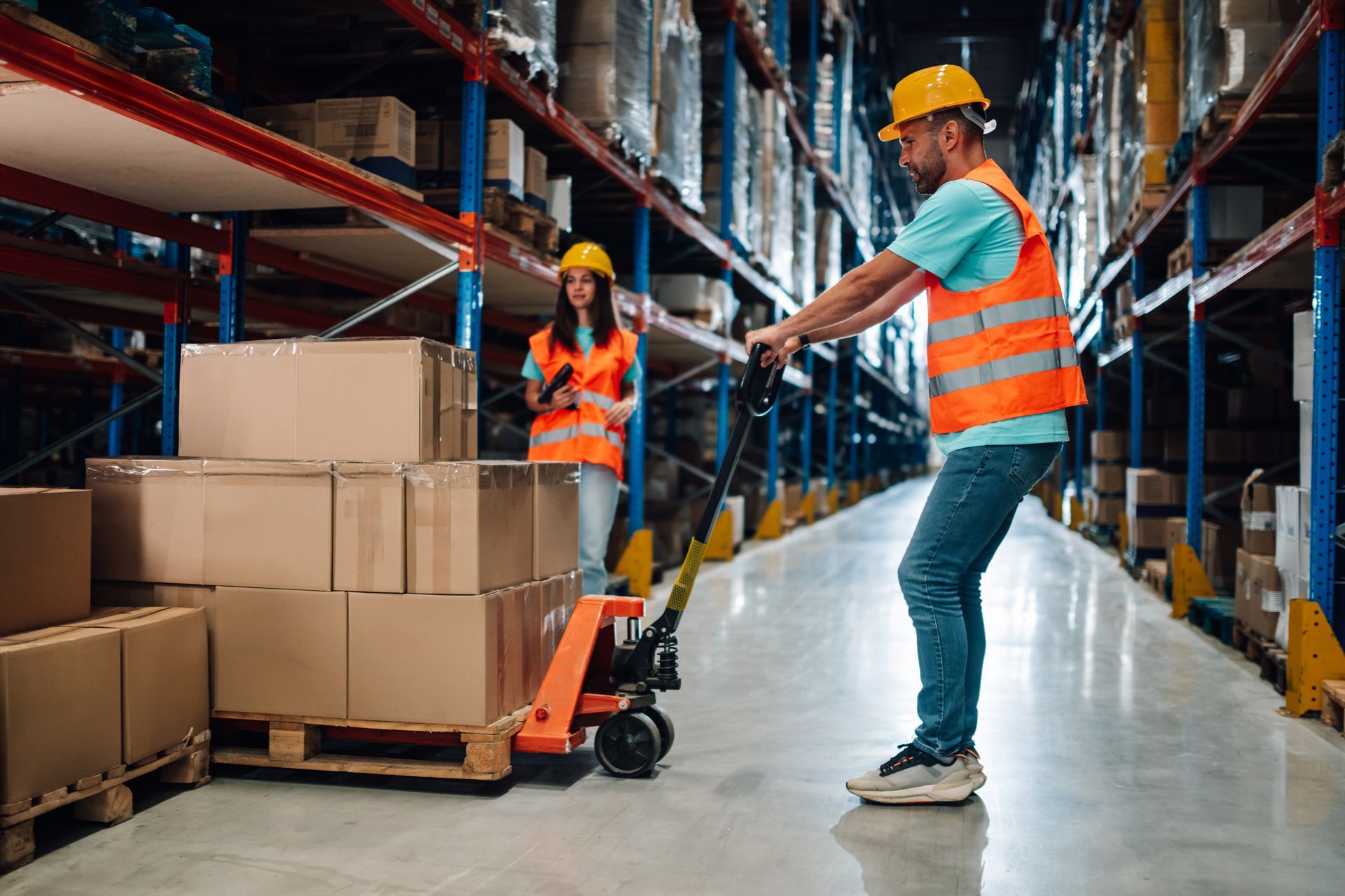Warehouse workers with a pallet jack, stacking boxes on shelves.