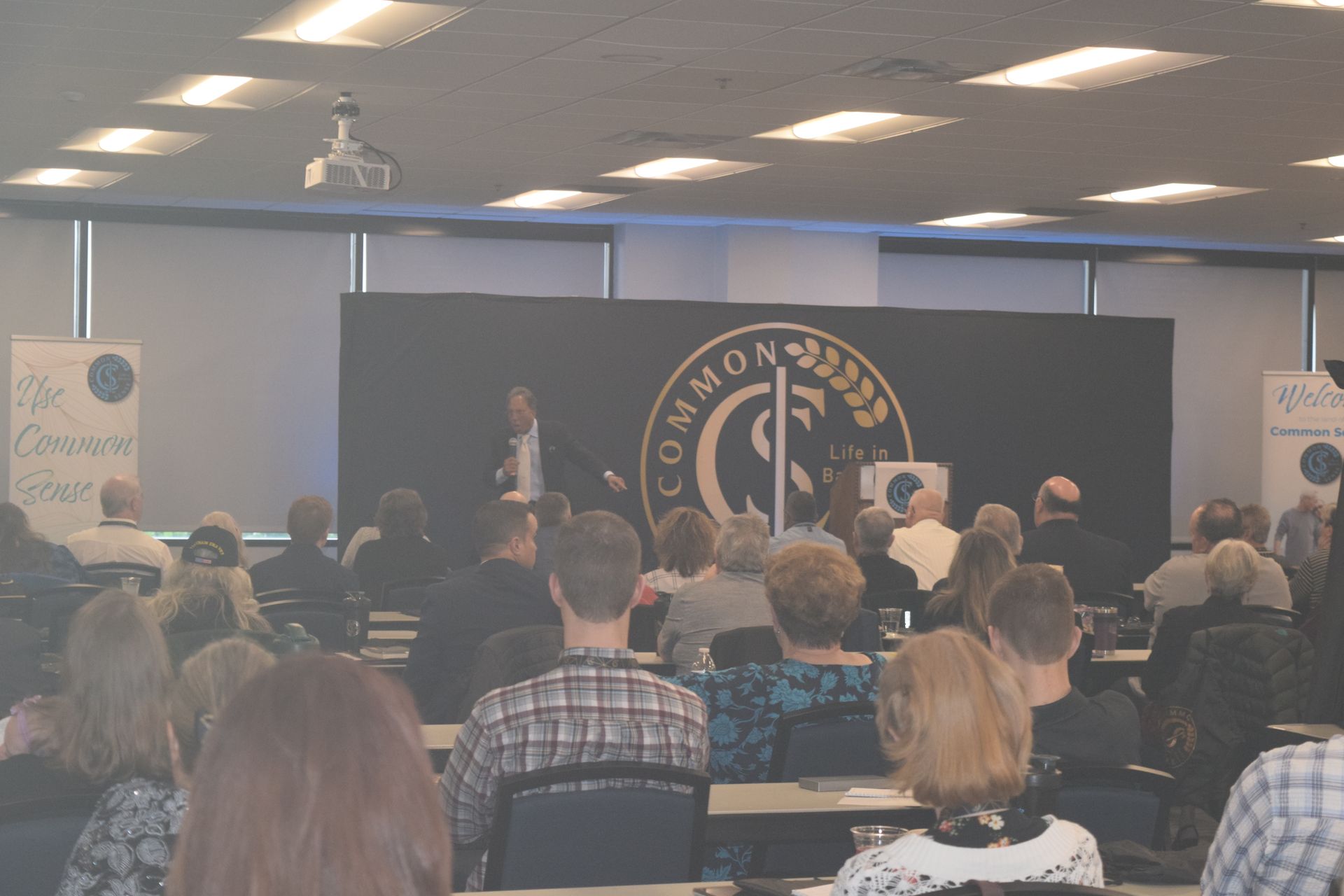 A group of people are sitting in front of a stage that says common