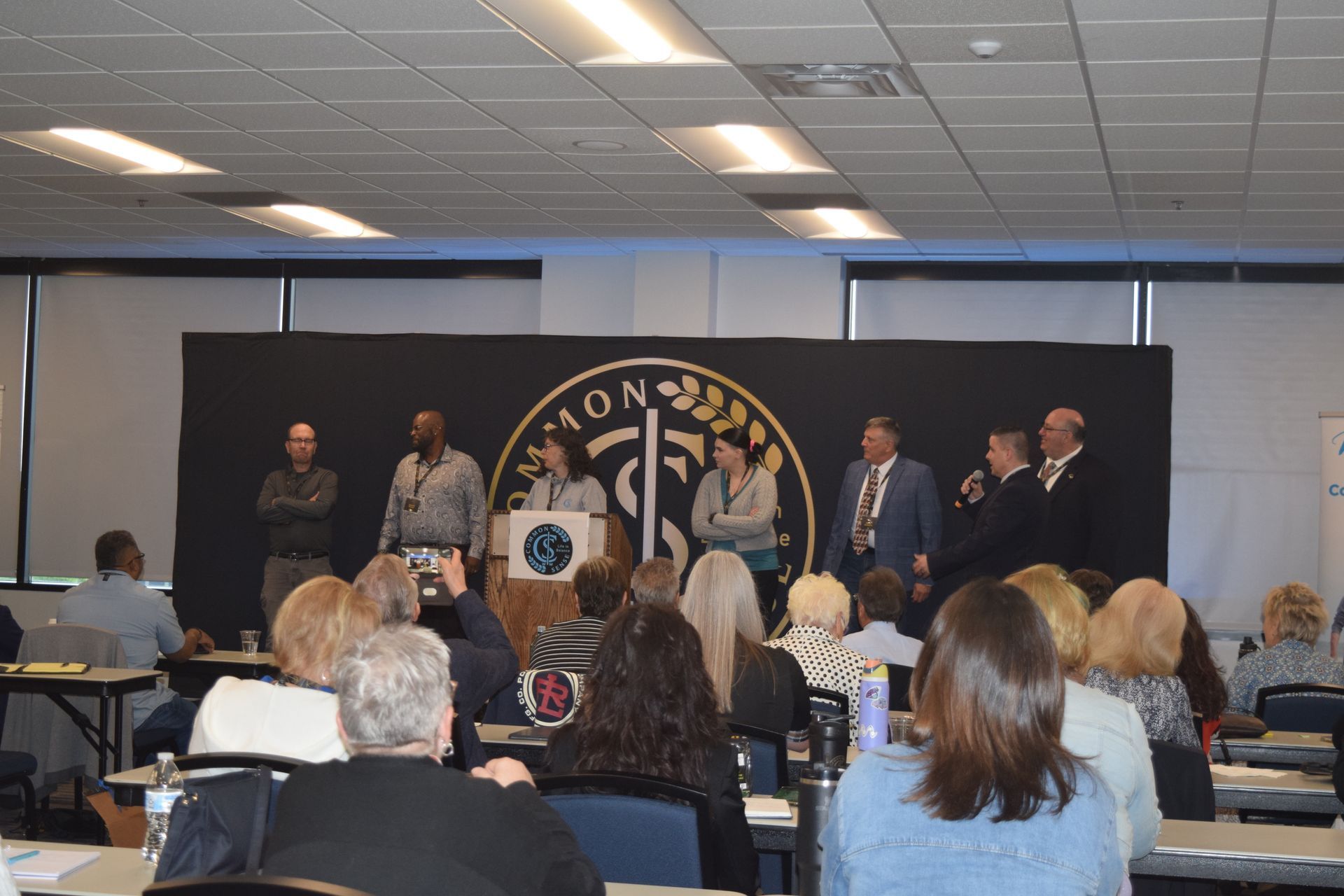 A group of people sitting at tables in front of a sign that says aon