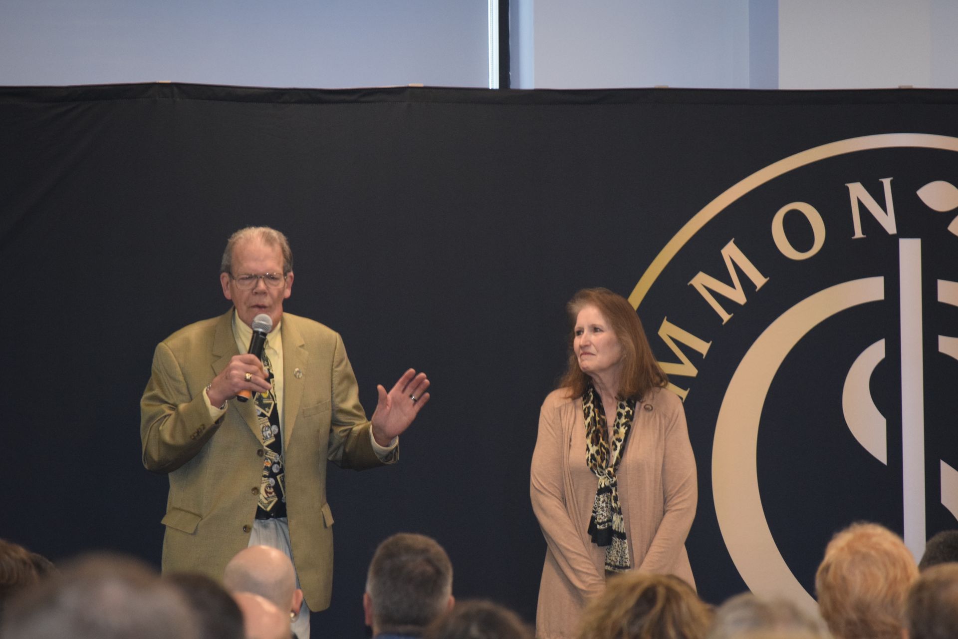 A man and a woman are standing in front of a crowd and talking into microphones.