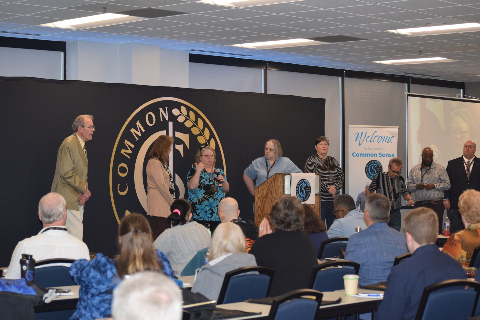 A group of people are sitting at tables in a room with a sign that says common
