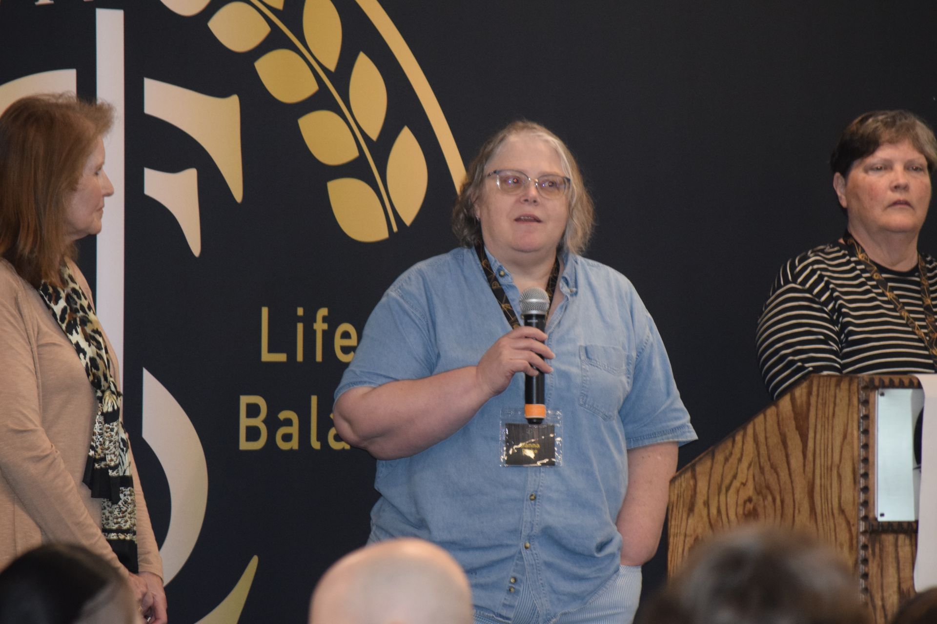 A woman is speaking into a microphone in front of a sign that says life bala