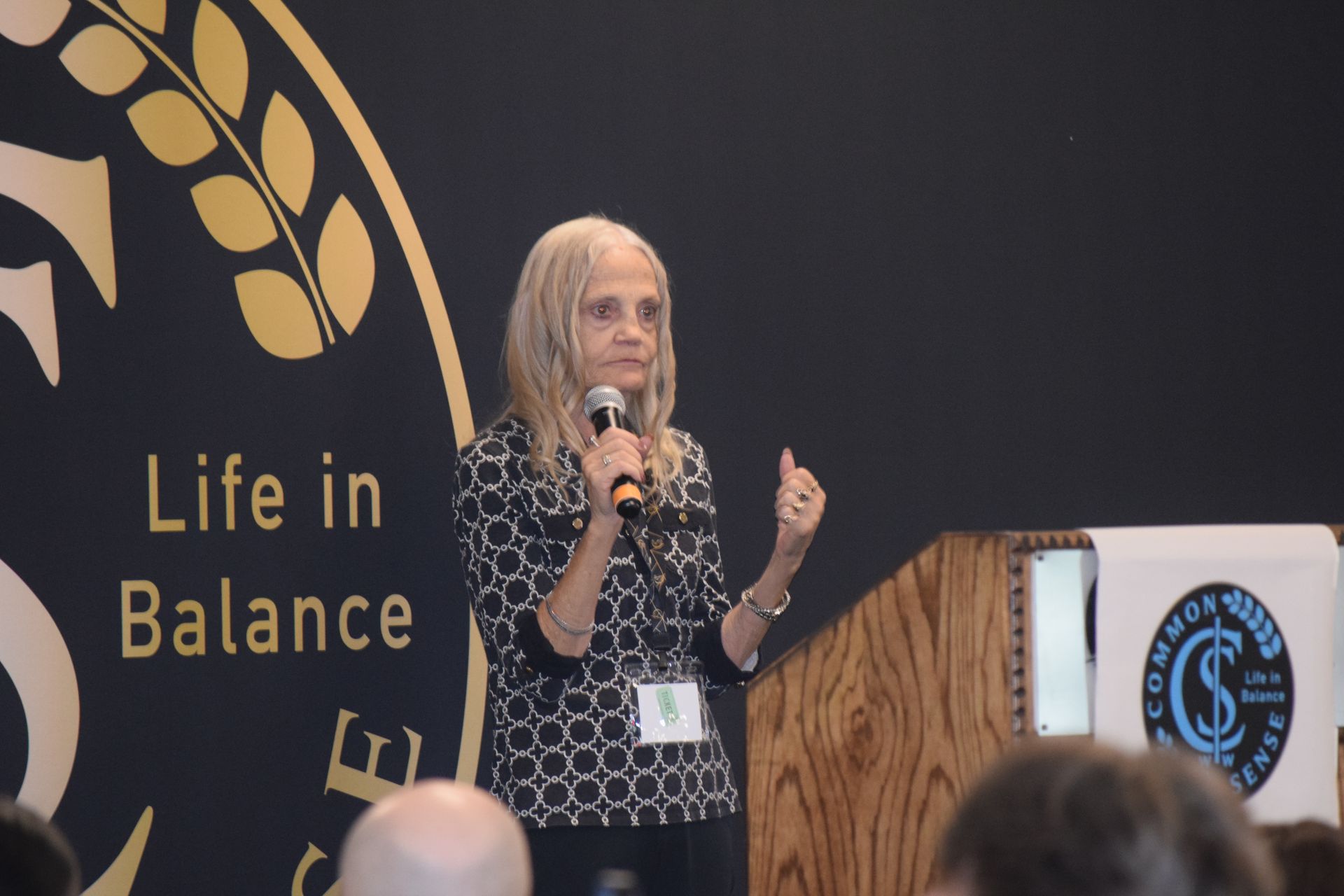 A woman is giving a speech in front of a sign that says life in balance