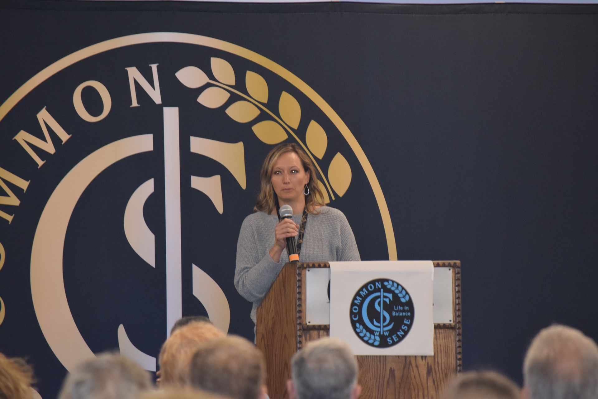 A woman is standing at a podium holding a microphone in front of a crowd.