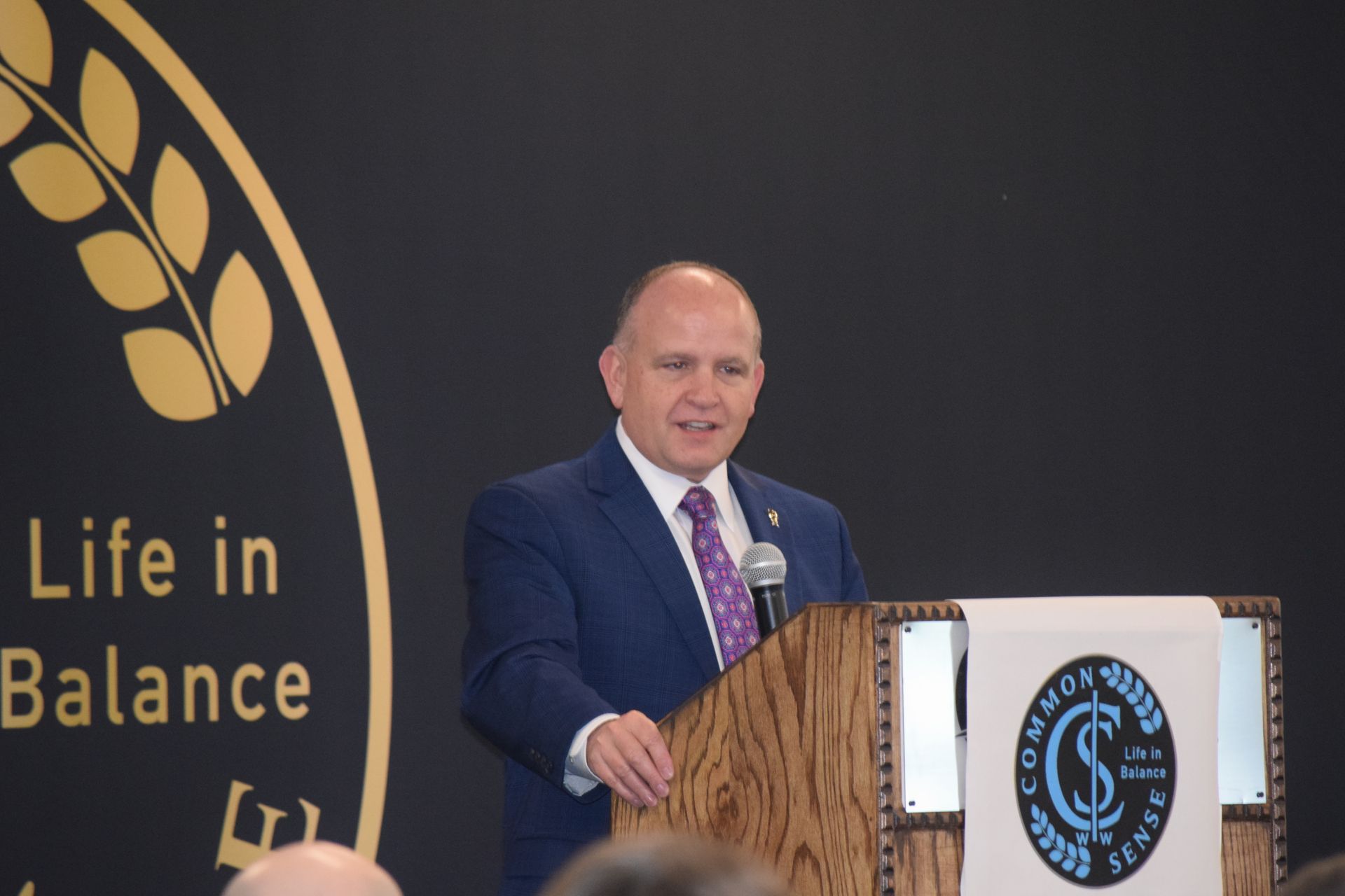 A man in a suit and tie is giving a speech at a podium that says life in balance