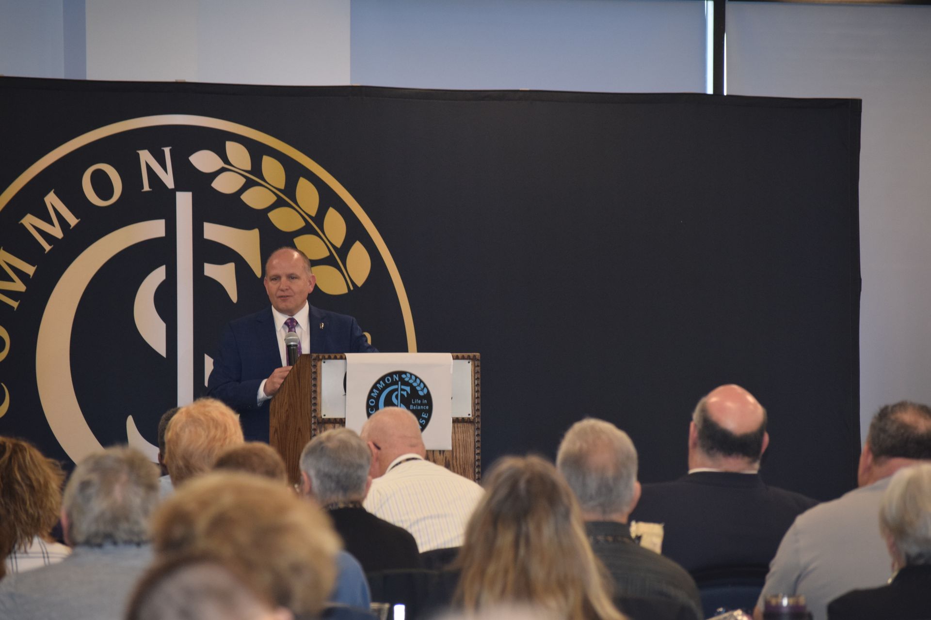 A man is giving a speech at a podium in front of a crowd of people.