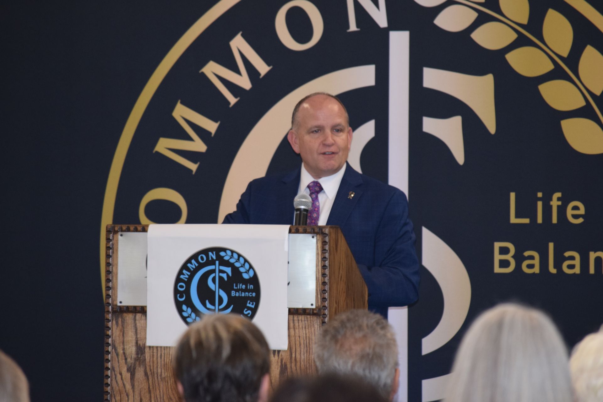 A man in a suit and tie is standing at a podium in front of a sign that says life balance