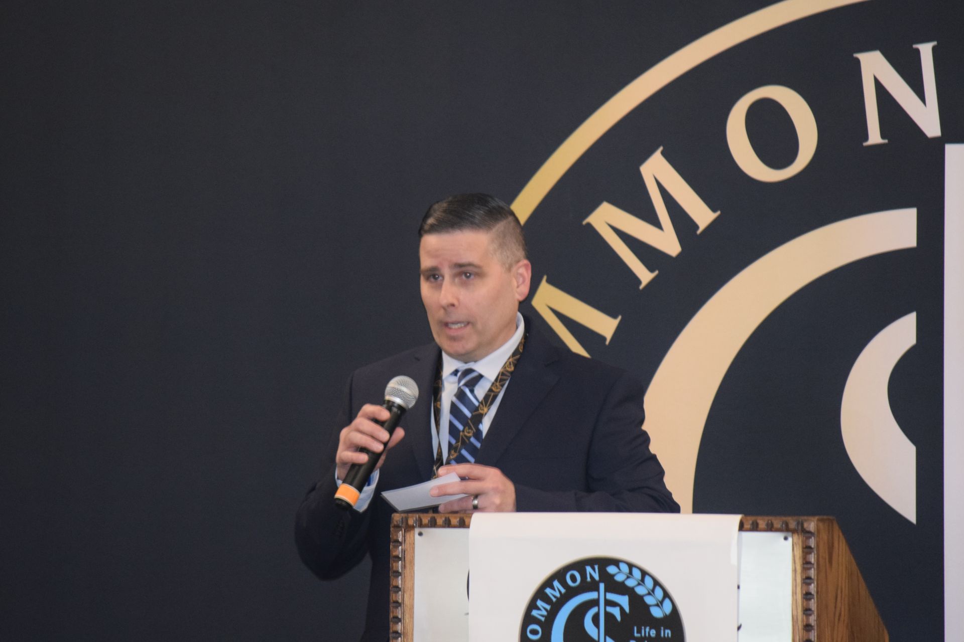 A man in a suit and tie is standing at a podium holding a microphone.