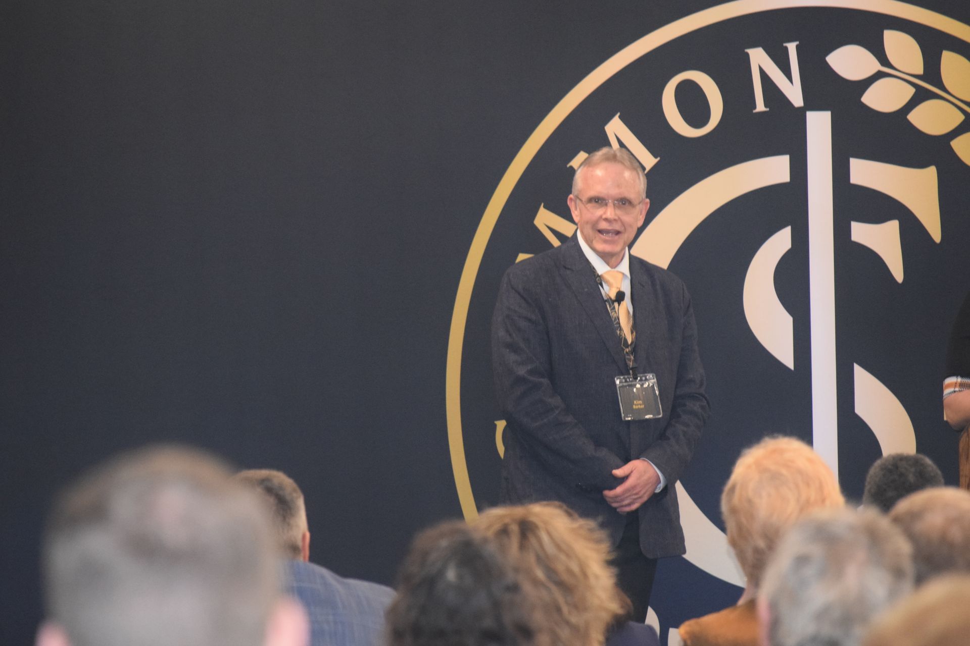 A man in a suit and tie is standing in front of a sign that says mon