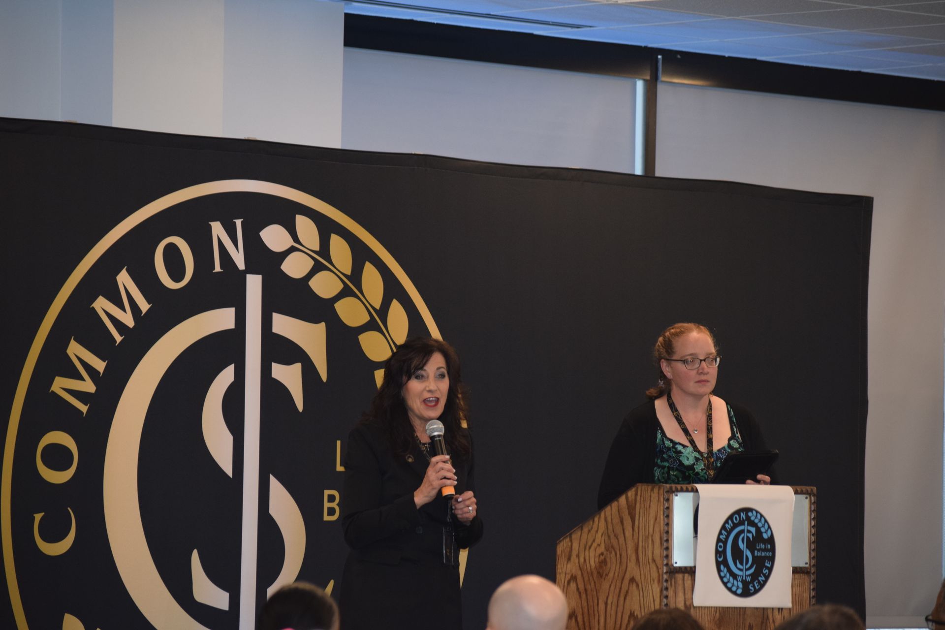 Two women stand at a podium in front of a sign that says common