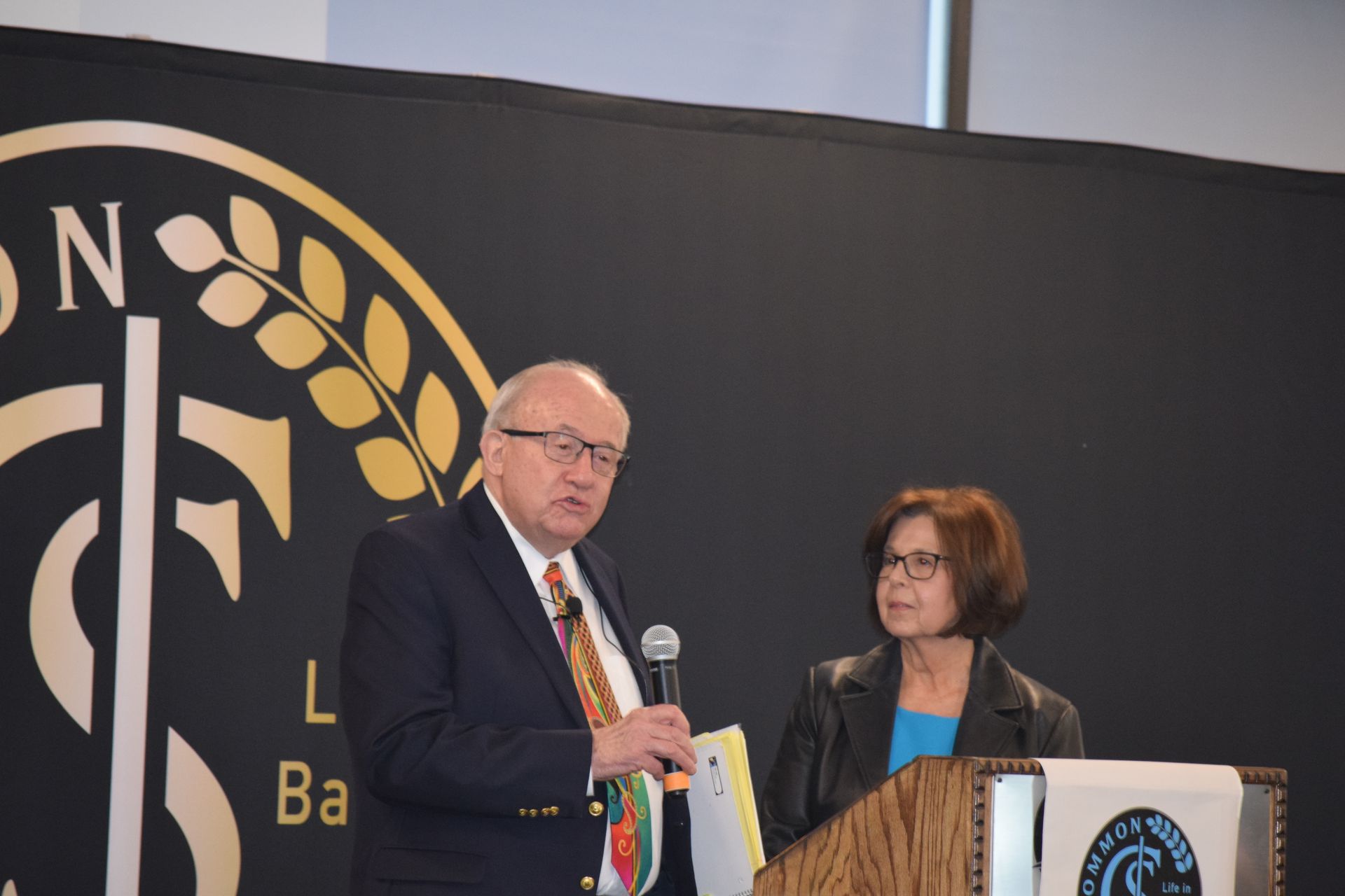 A man and a woman are standing at a podium talking into microphones.