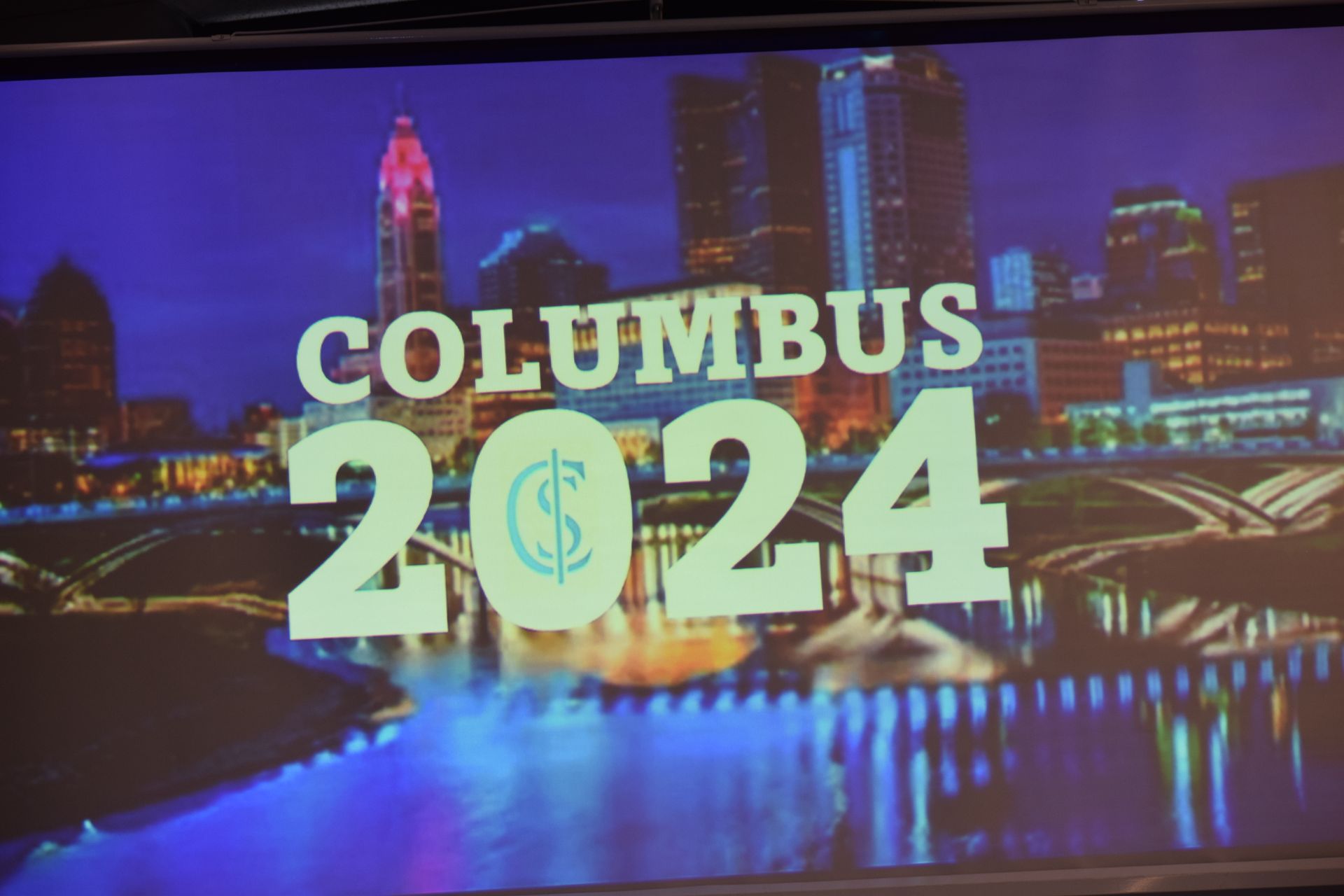 A projector screen shows a picture of columbus 2024