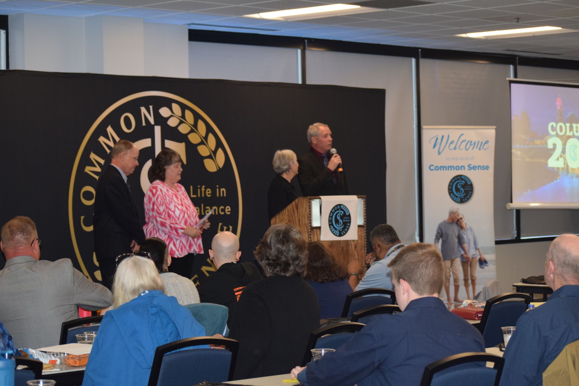 A group of people sitting at tables in front of a sign that says common
