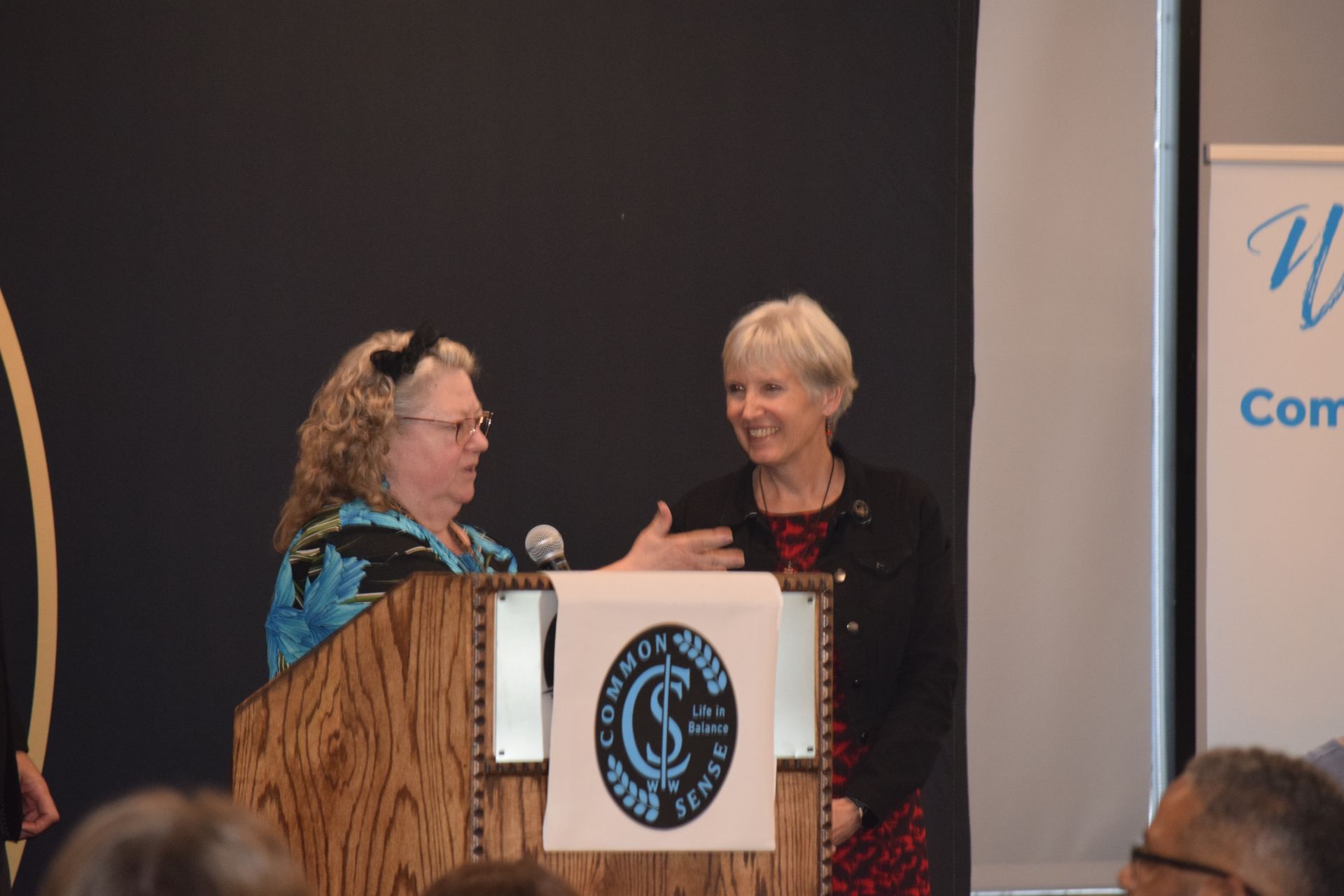 Two women are standing at a podium talking to each other.