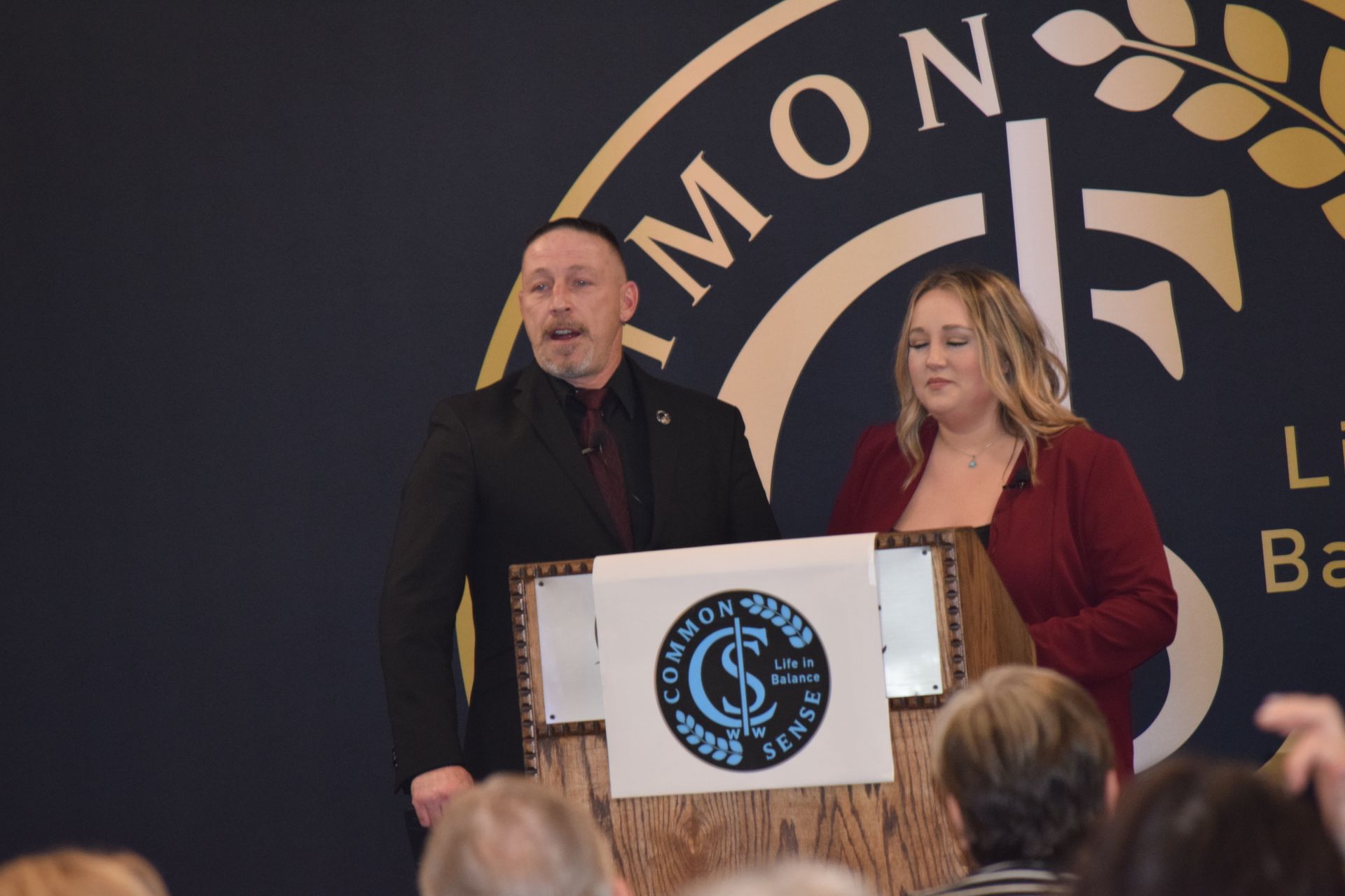 A man and a woman stand at a podium with a sign that says simon