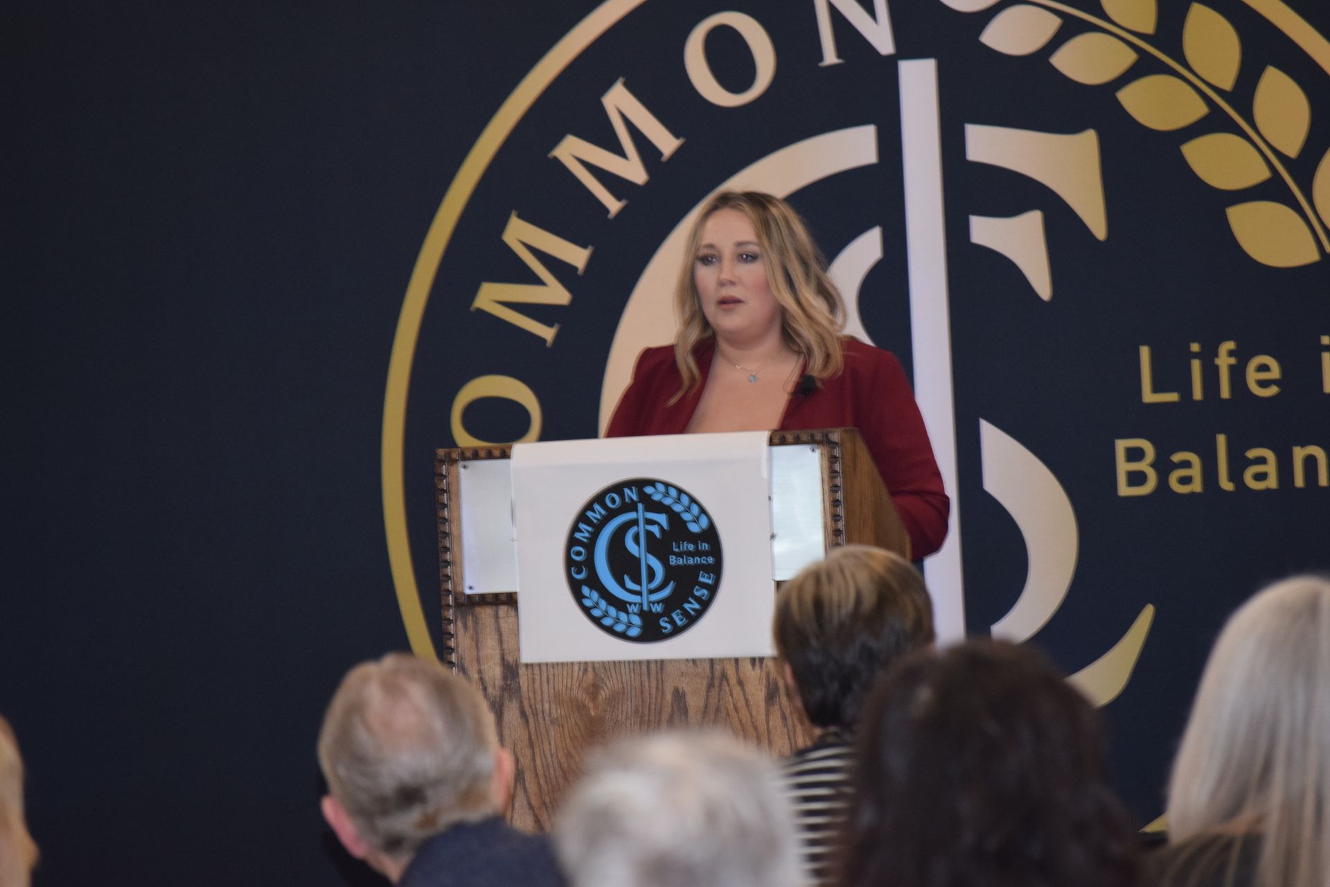 A woman stands at a podium in front of a sign that says life balance