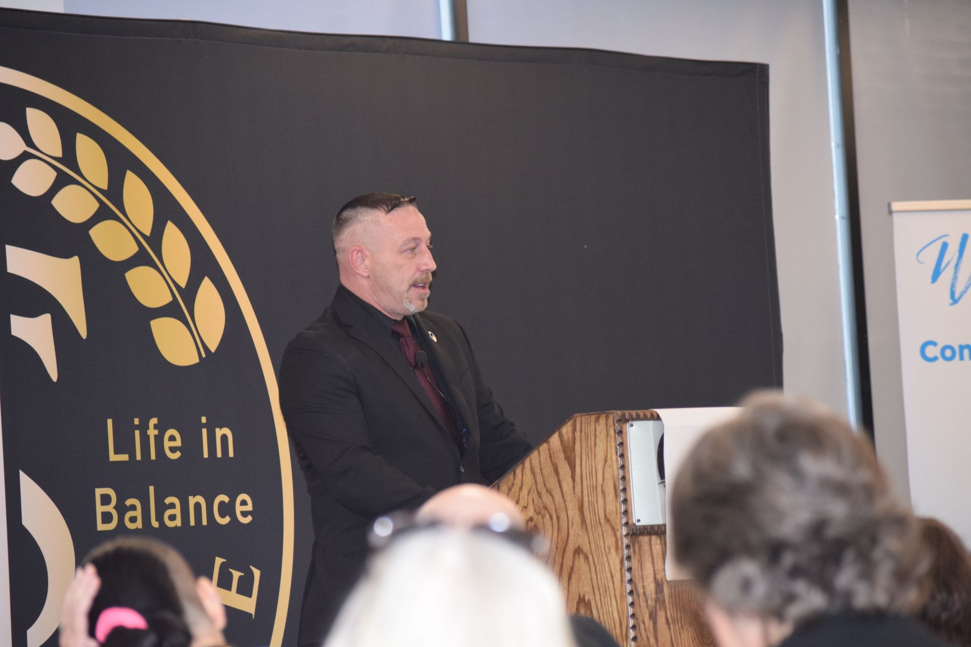 A man stands at a podium in front of a sign that says life in balance