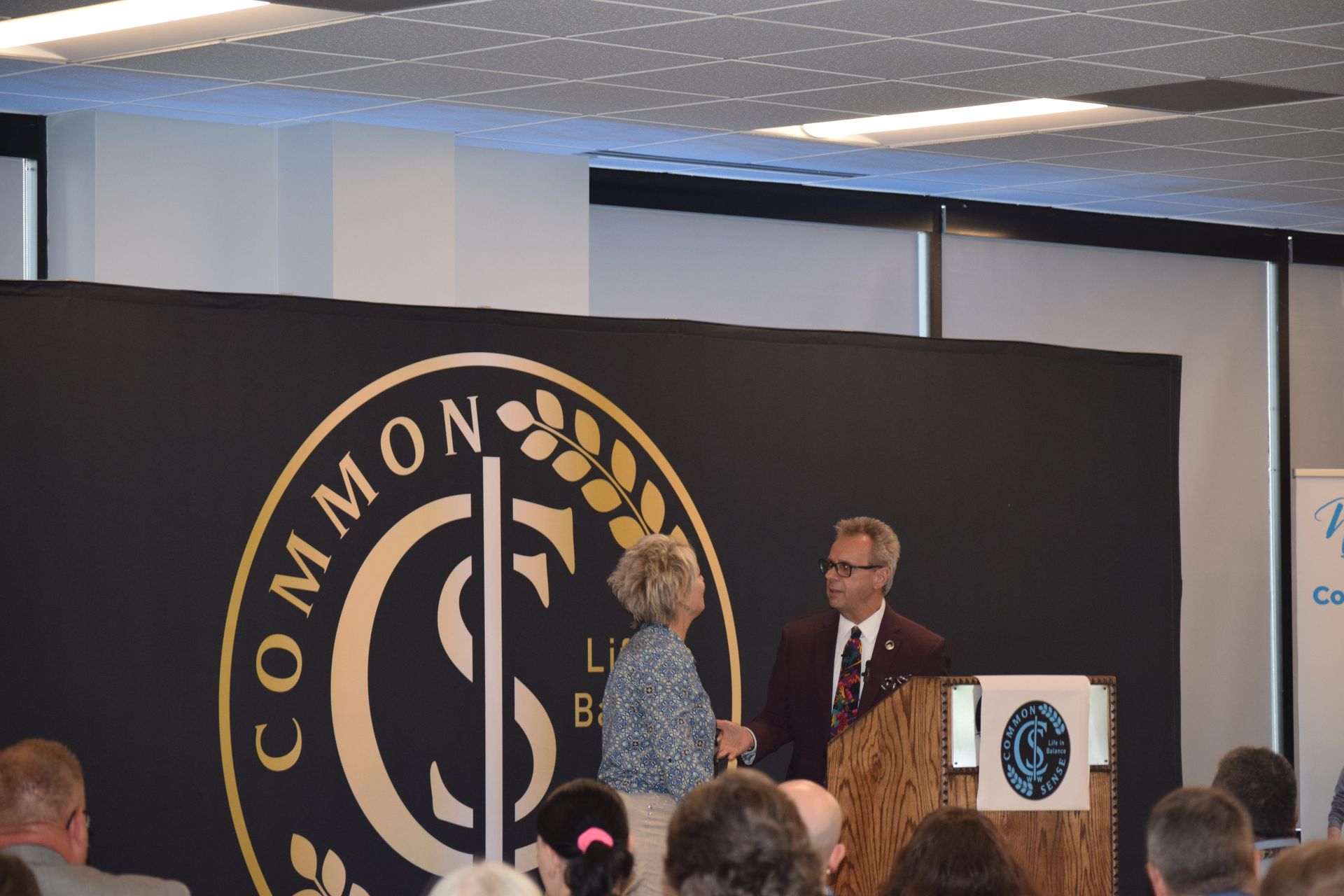 A man stands at a podium in front of a wall that says common