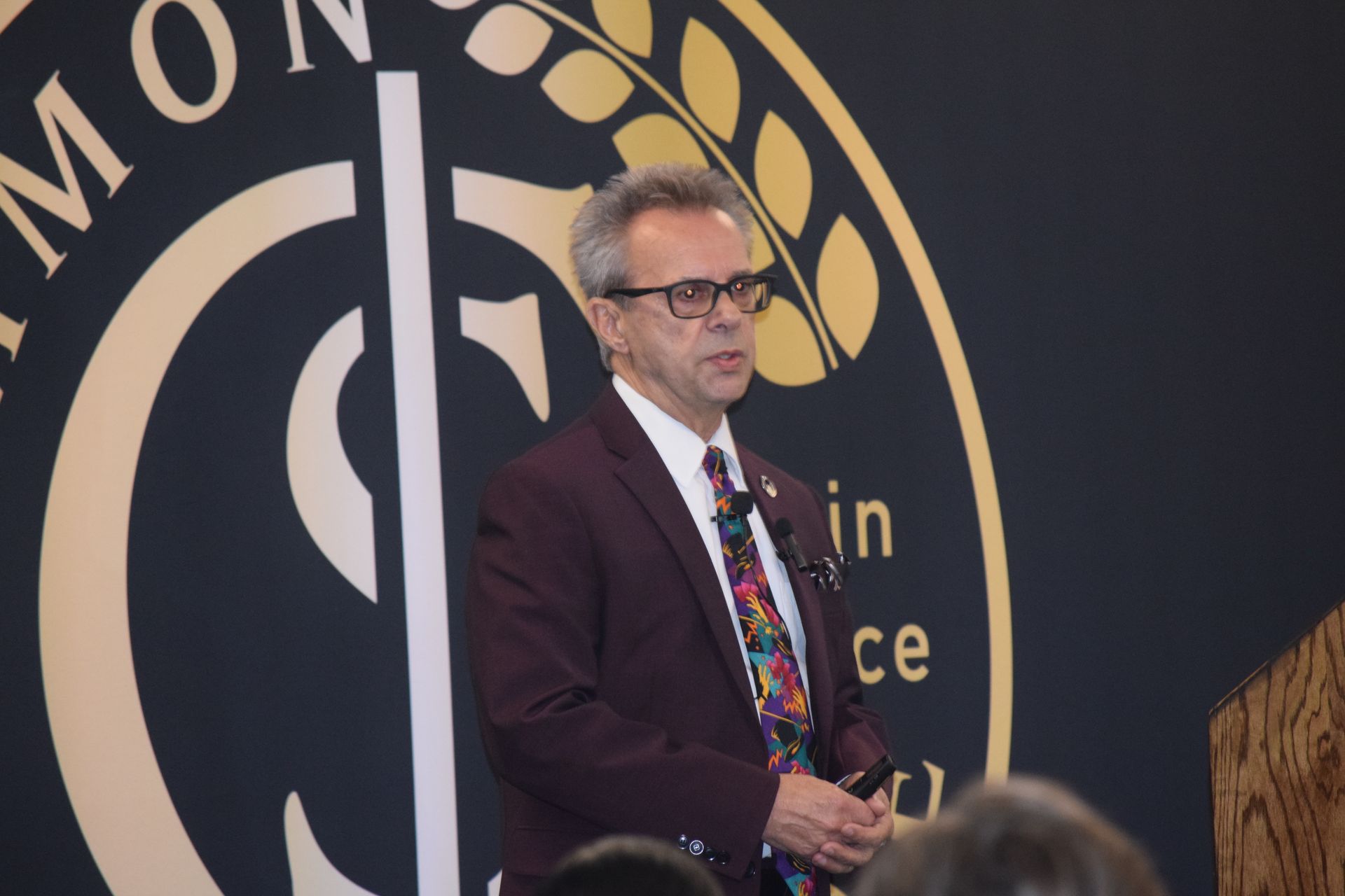 A man in a suit and tie is giving a speech in front of a logo.