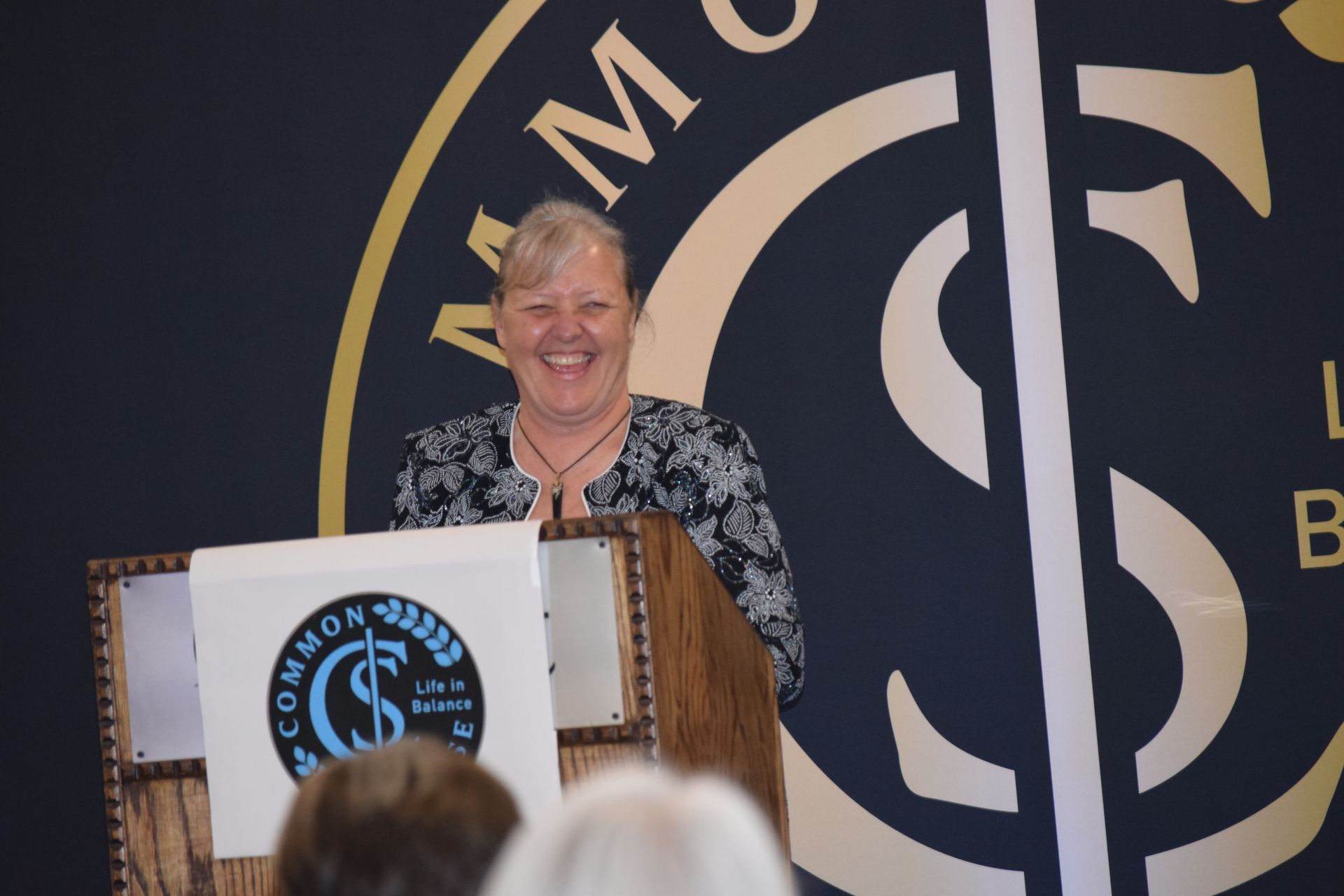 A woman stands at a podium in front of a sign that says common