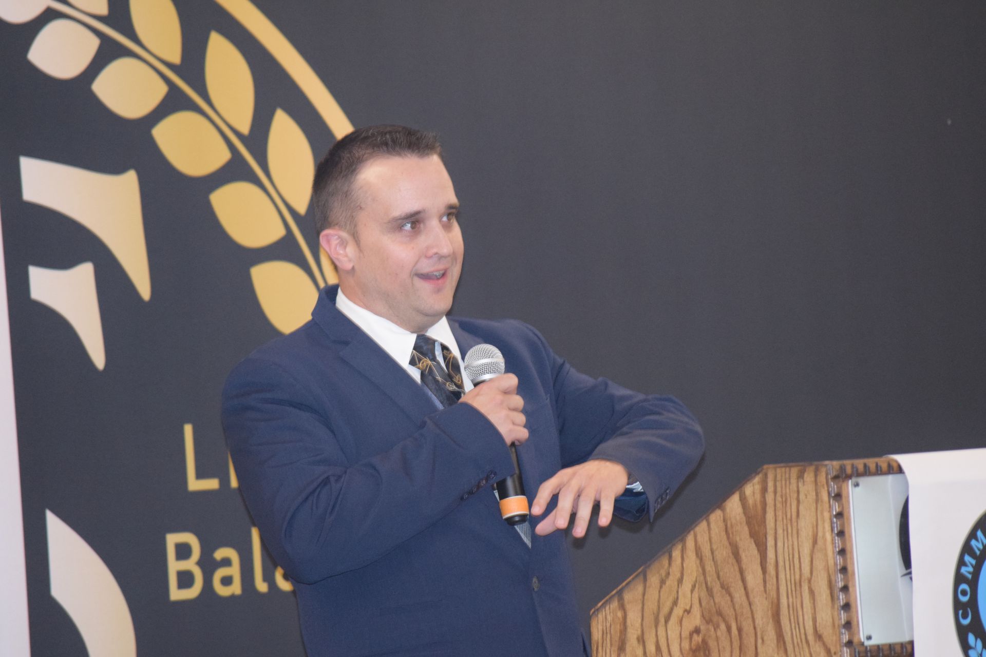 A man in a suit and tie is standing at a podium holding a microphone.