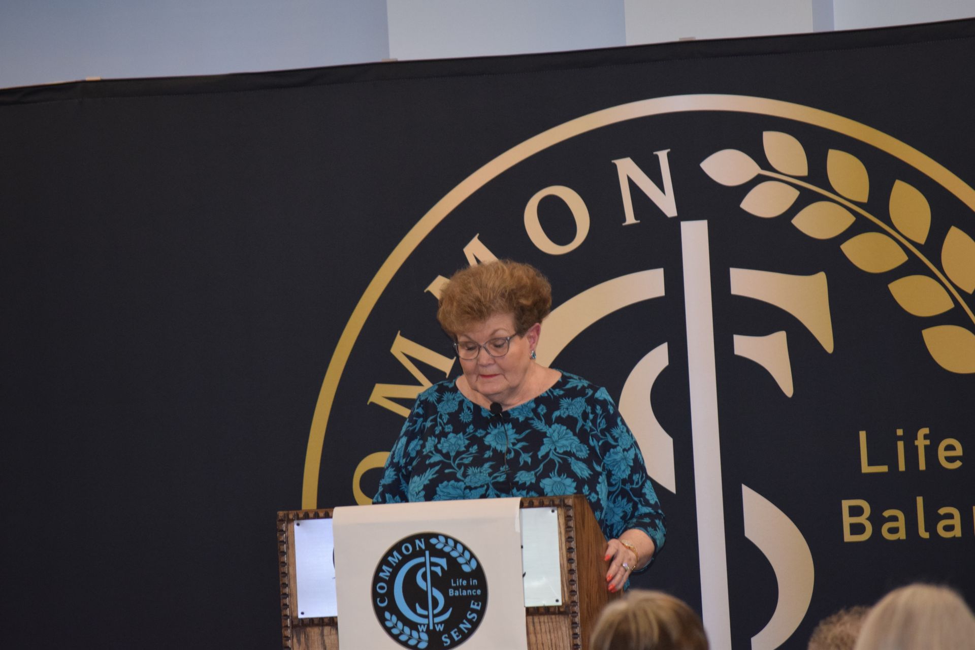 A woman stands at a podium in front of a banner that says common life