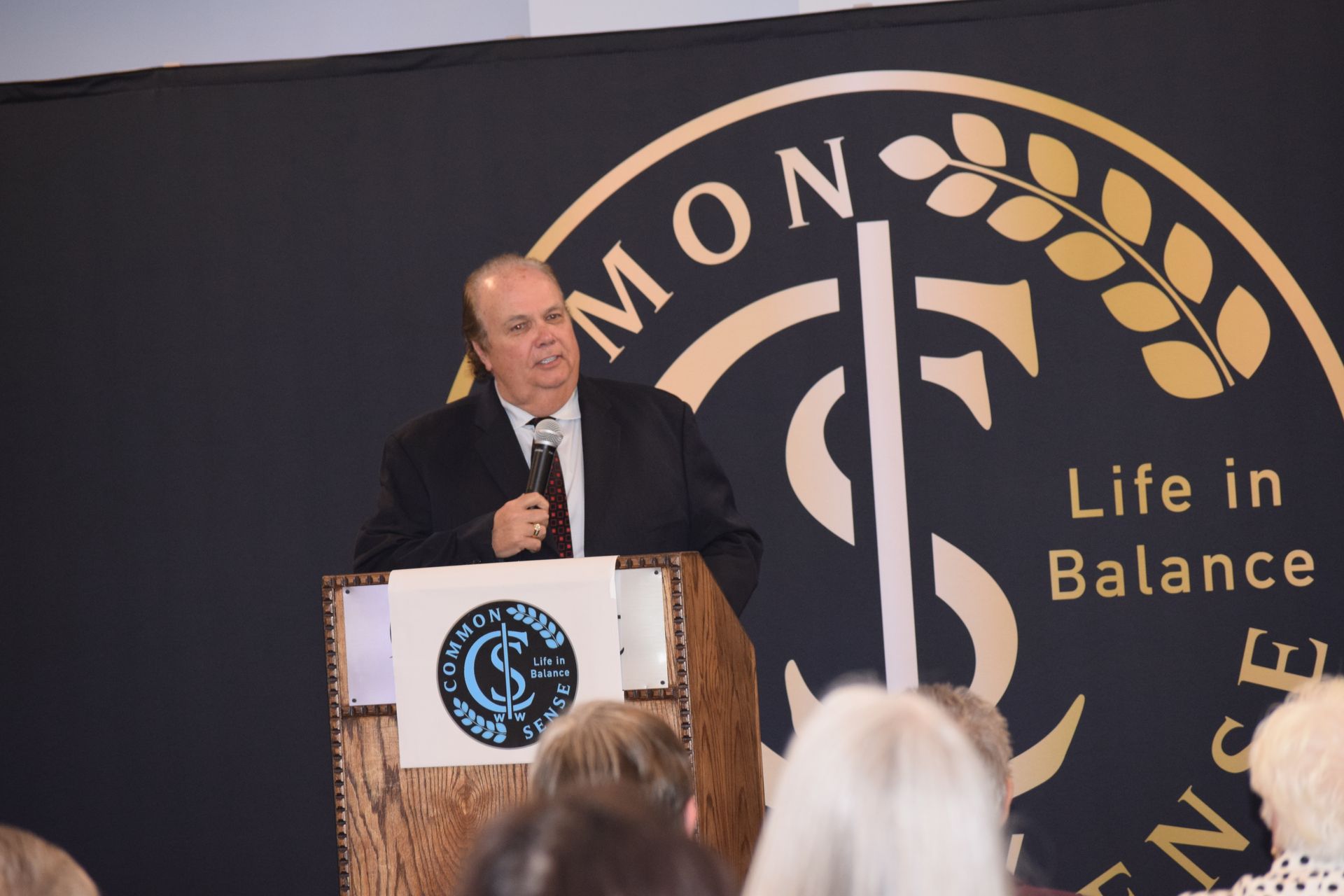 A man stands at a podium in front of a sign that says life in balance
