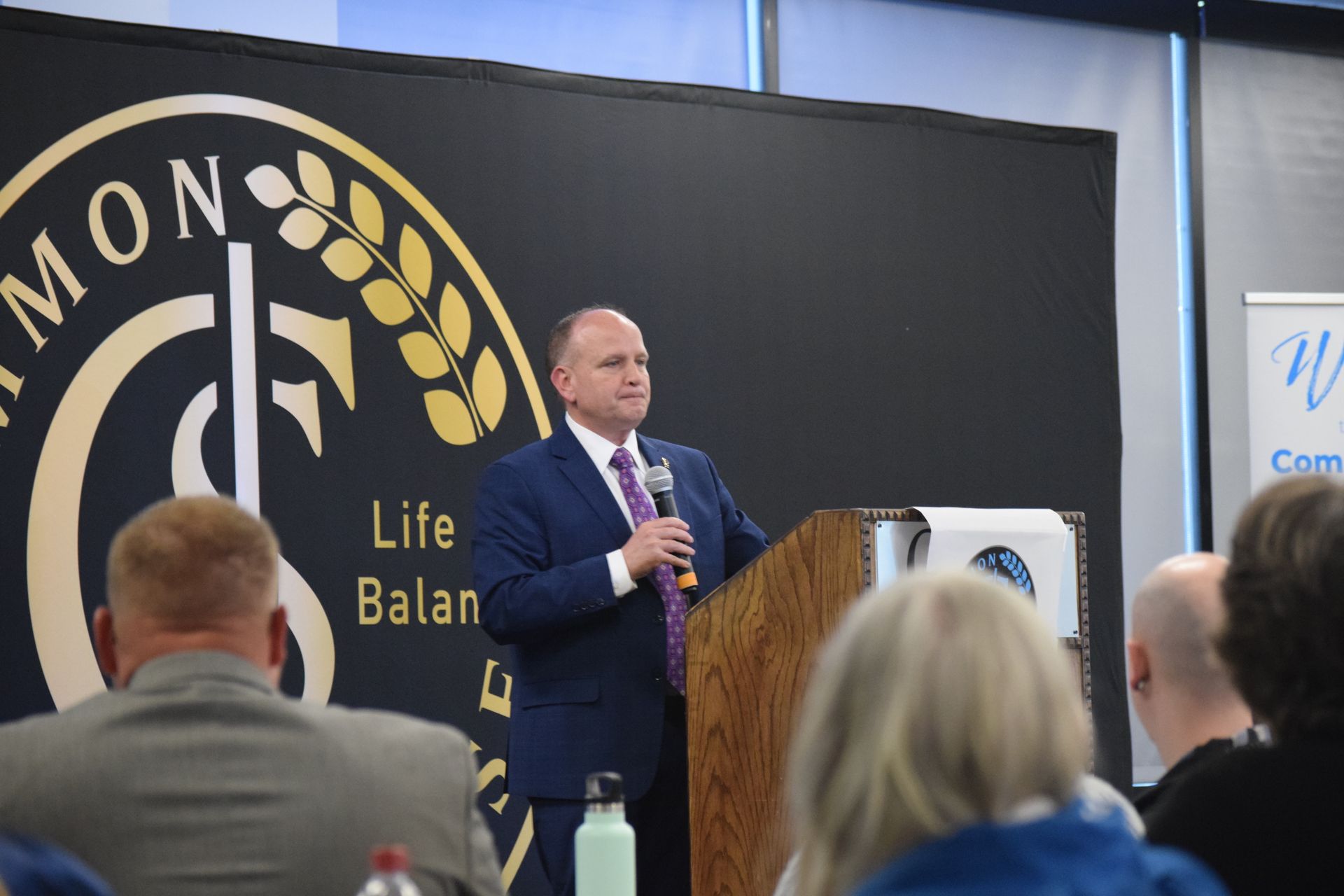 A man in a suit and tie is standing at a podium giving a speech to a group of people.