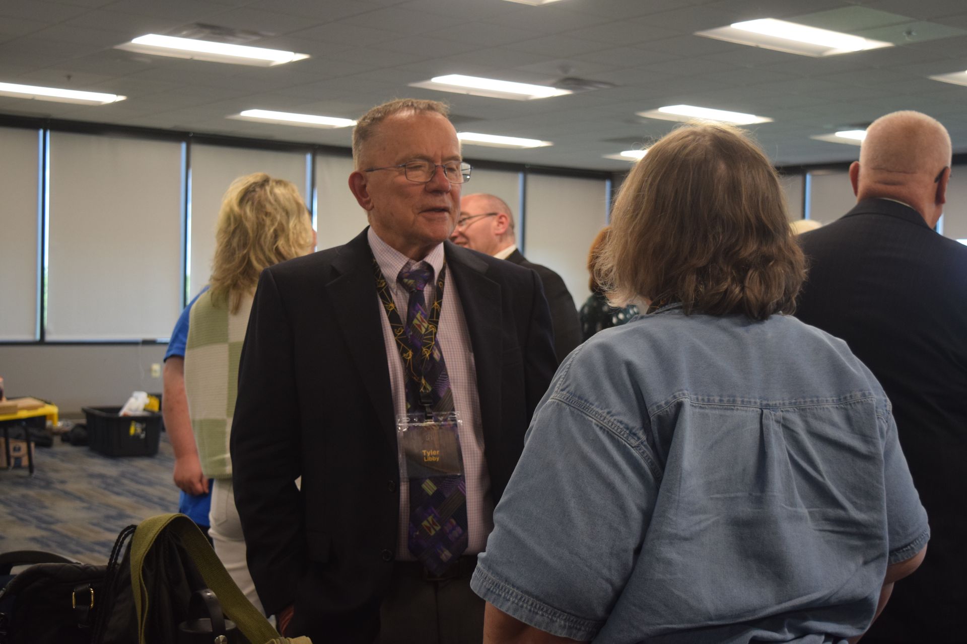 A man in a suit and tie is talking to a woman in a blue shirt.