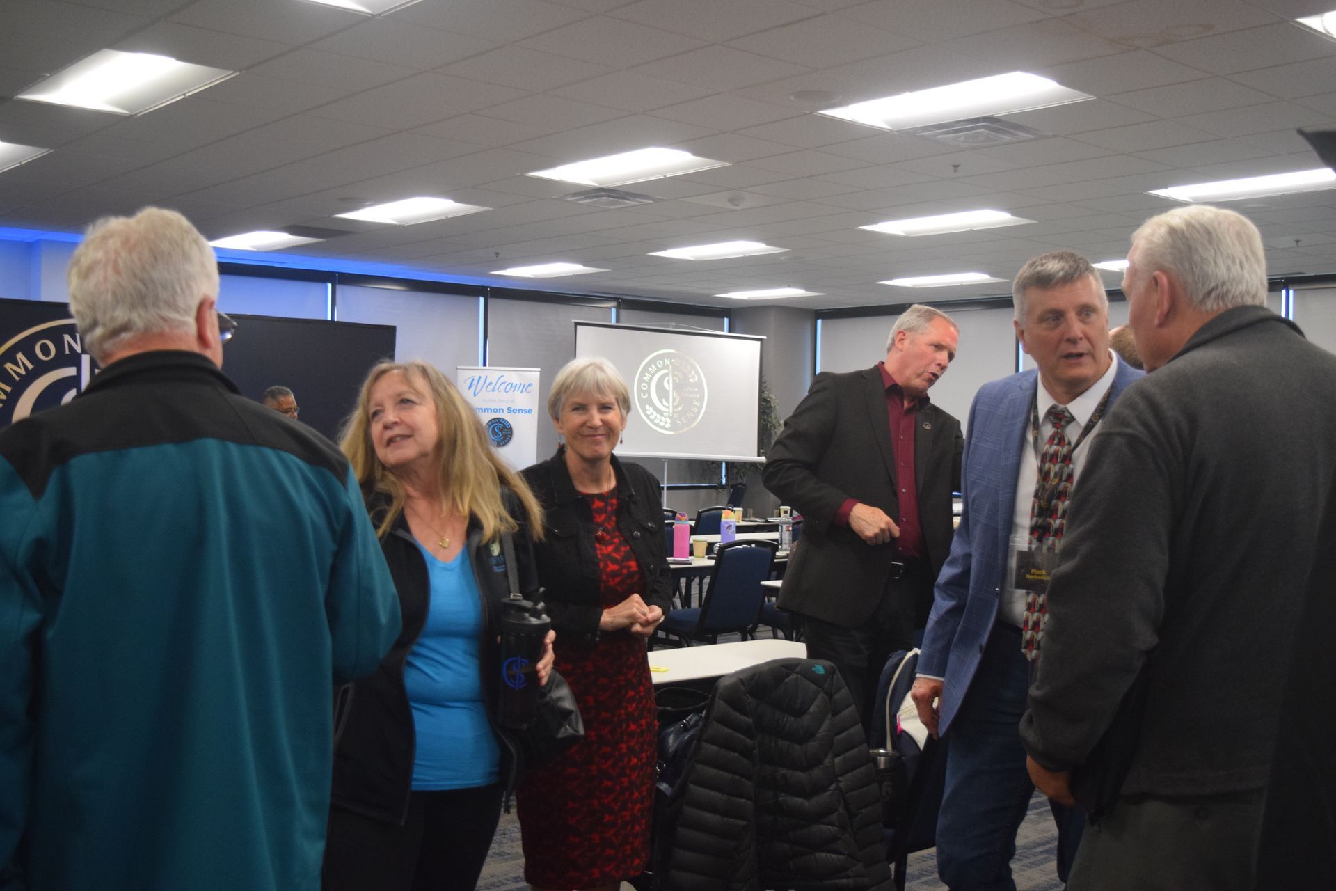 A group of people are standing in a room talking to each other.
