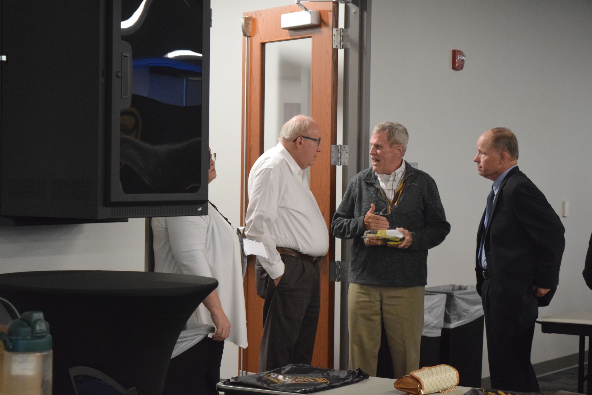 A group of men are standing in a room talking to each other.