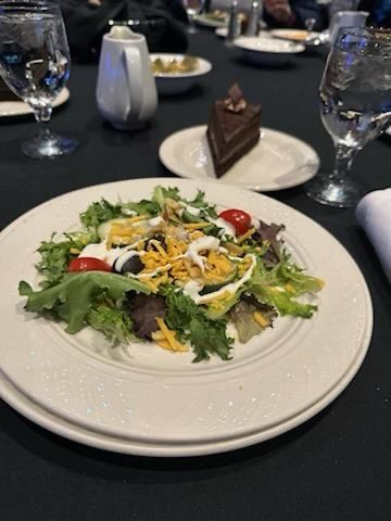A white plate topped with a salad and a piece of cake on a table.