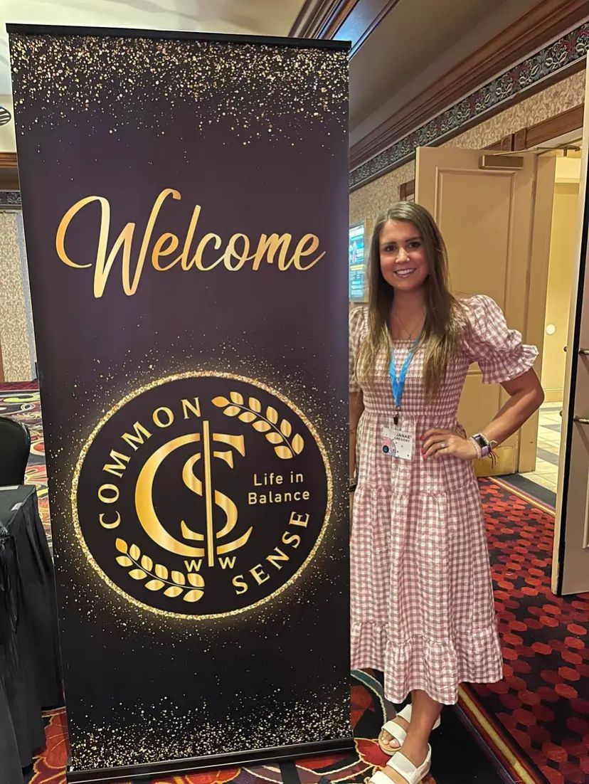 A woman is standing in front of a sign that says welcome