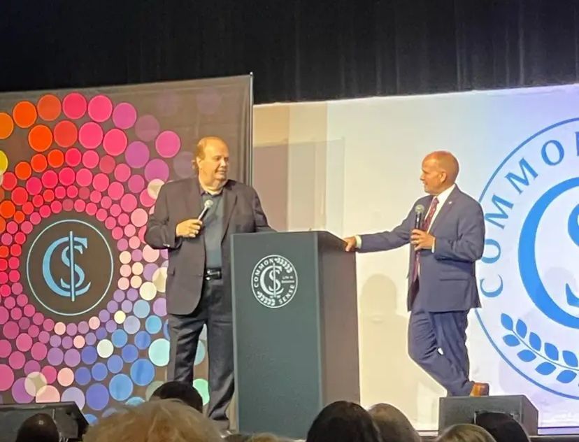 Two men are standing at a podium with microphones in front of a crowd.