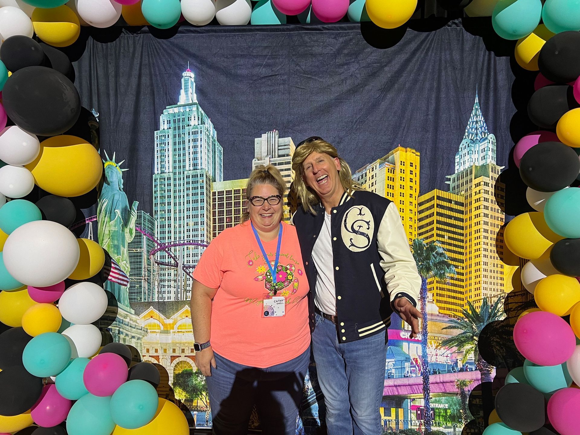 Two people are posing for a picture in front of a wall of balloons.