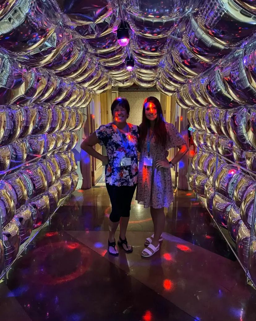Two women are standing in a tunnel filled with balloons.